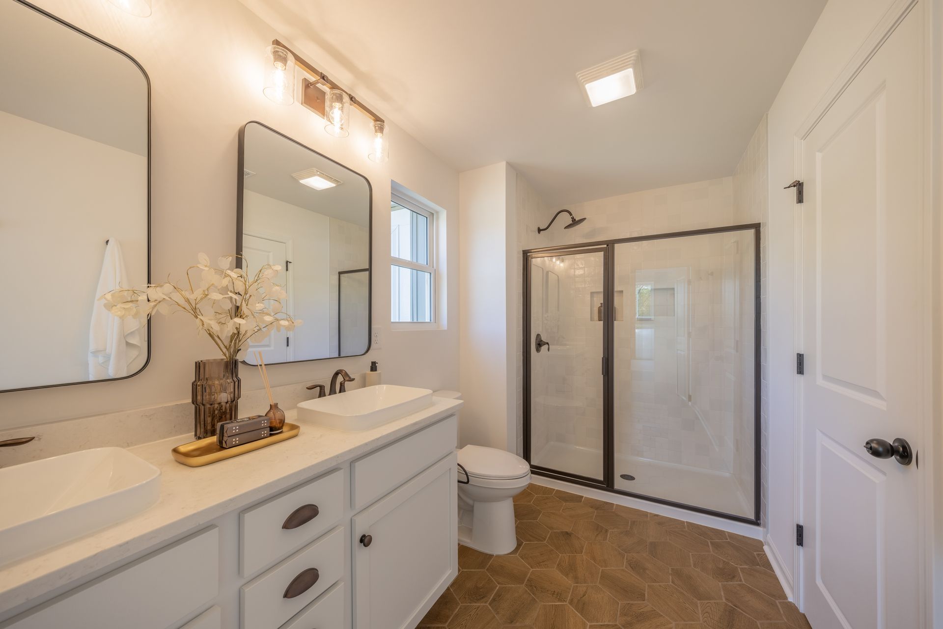 A bathroom with two sinks , a toilet , and a walk in shower - Abigale Floorplan by True Homes.