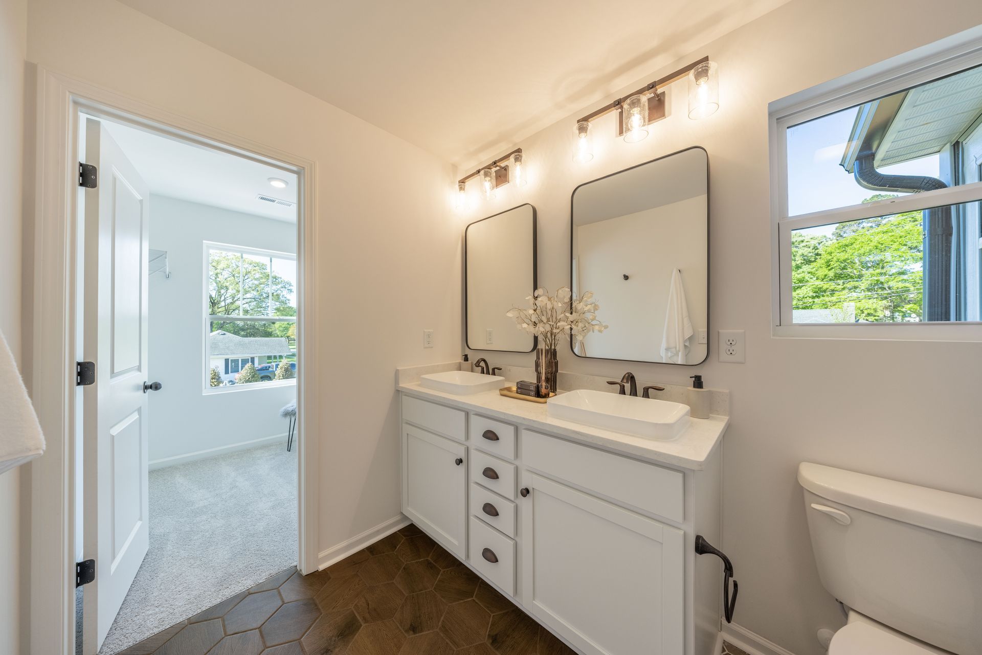 A bathroom with two sinks , two mirrors , a toilet and a window - Abigale Floorplan by True Homes.