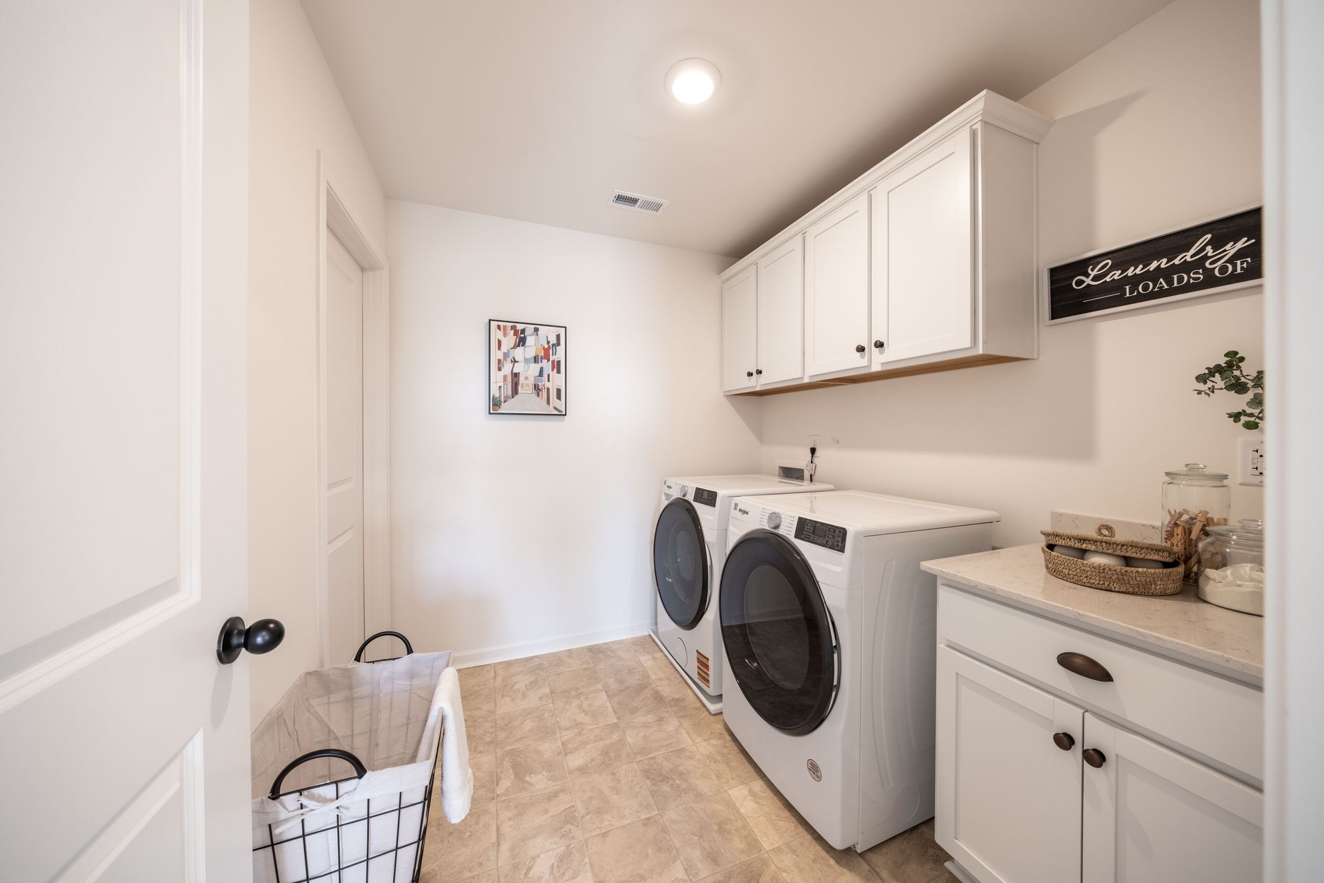 A laundry room with a washer and dryer and a laundry basket - Abigale Floorplan by True Homes.