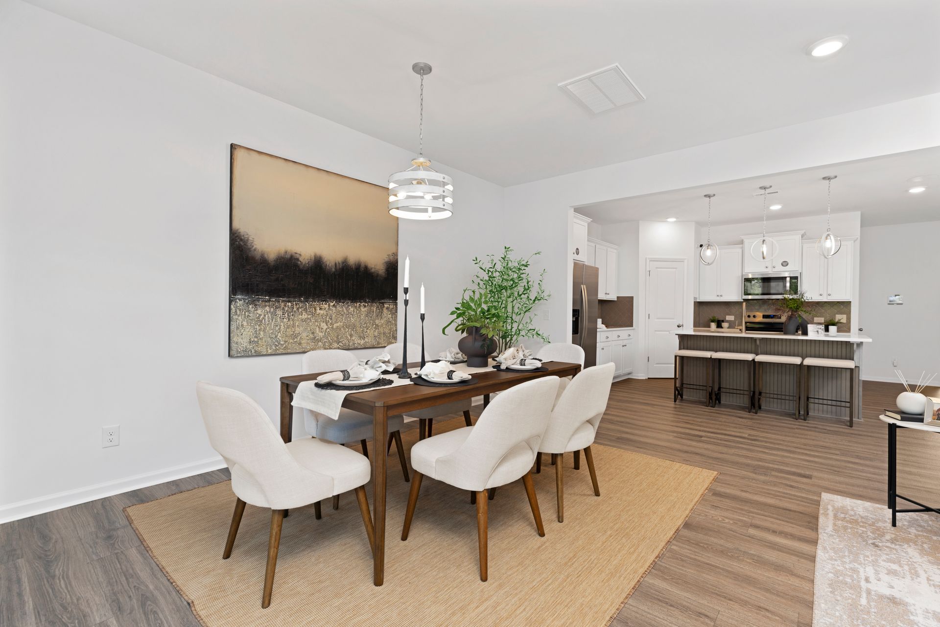 A dining room with a table and chairs and a painting on the wall.