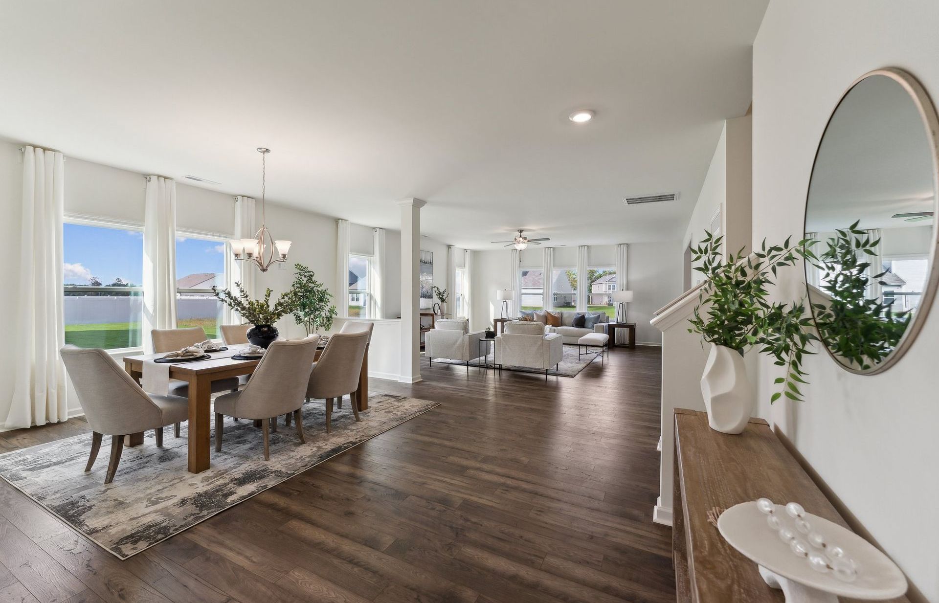 Open-concept dining and living area with a wood floor, white walls, and large windows.