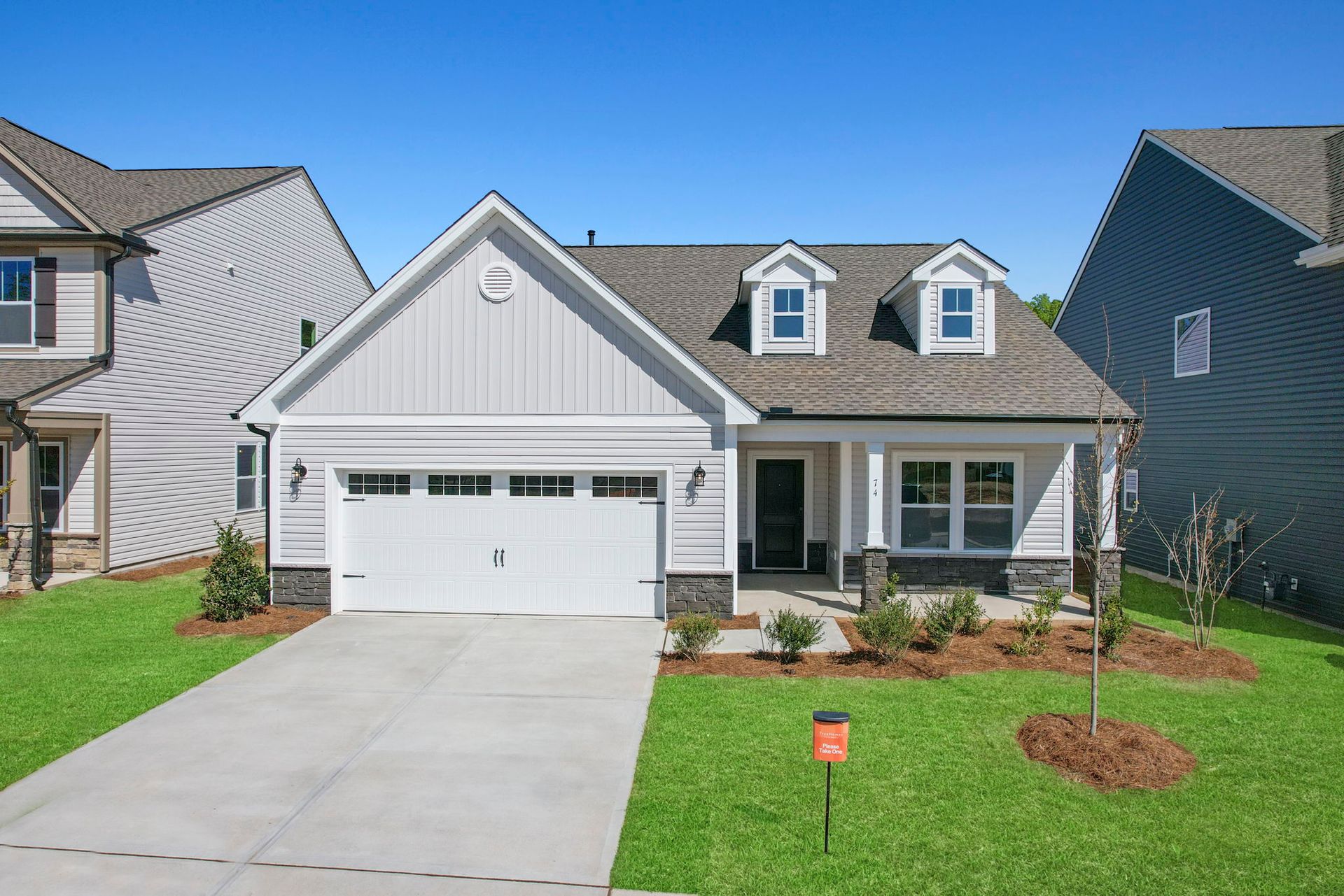A white house with a gray roof and a white garage door is sitting on top of a lush green lawn.