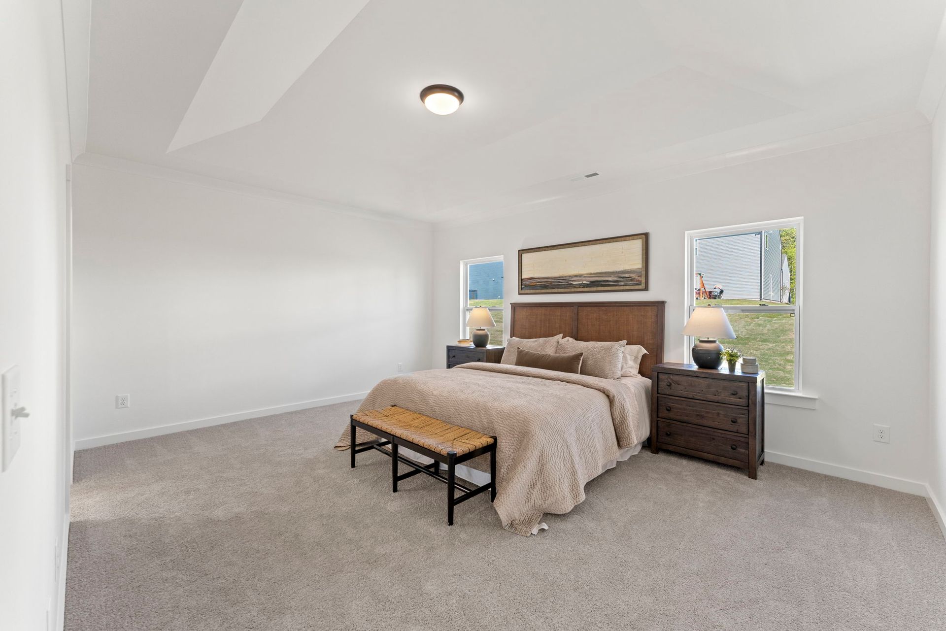 A bedroom with a bed , dresser , nightstand and two windows.