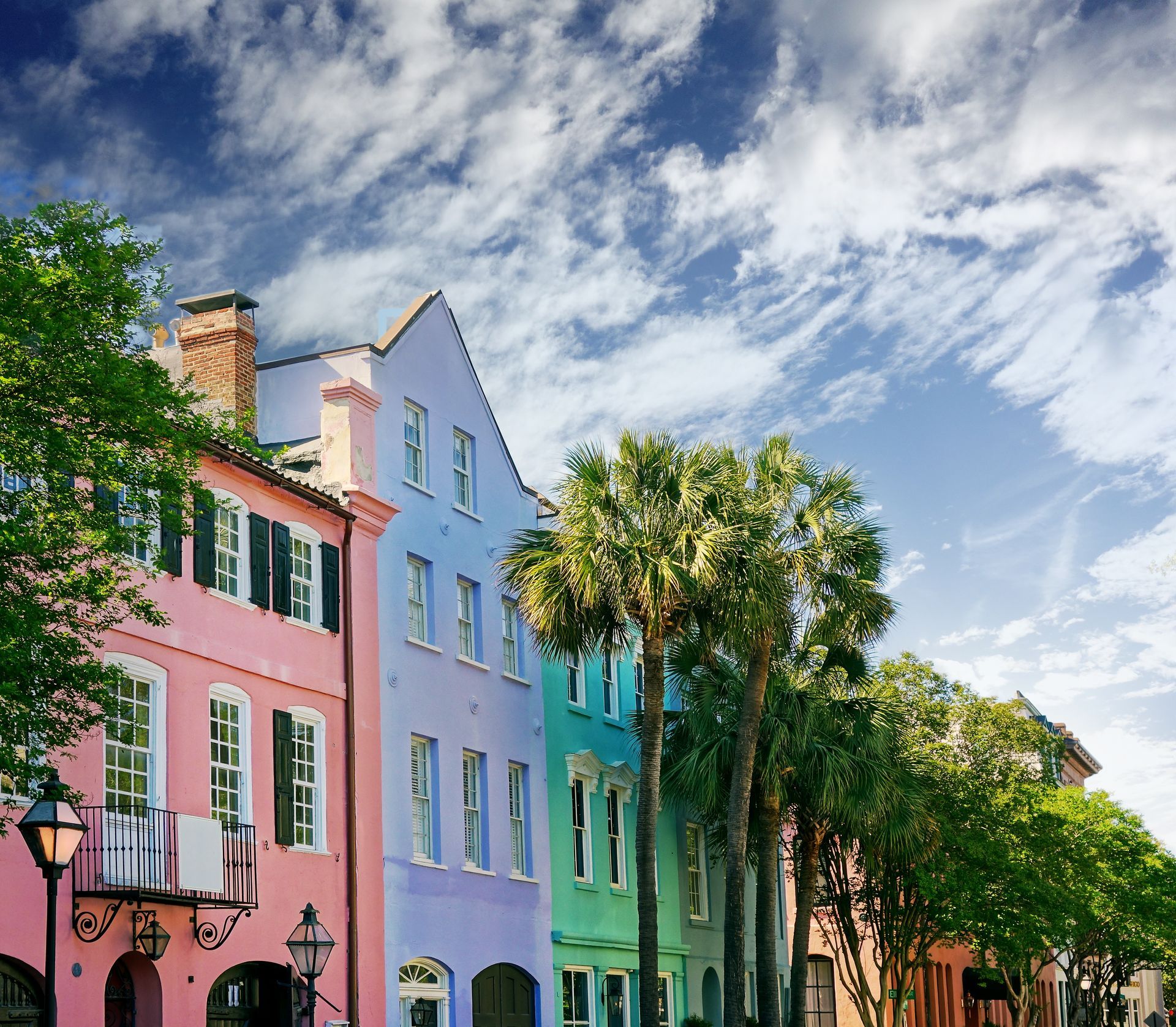 Colorful row houses with shutters and palm trees under a partly cloudy sky in Charleston.