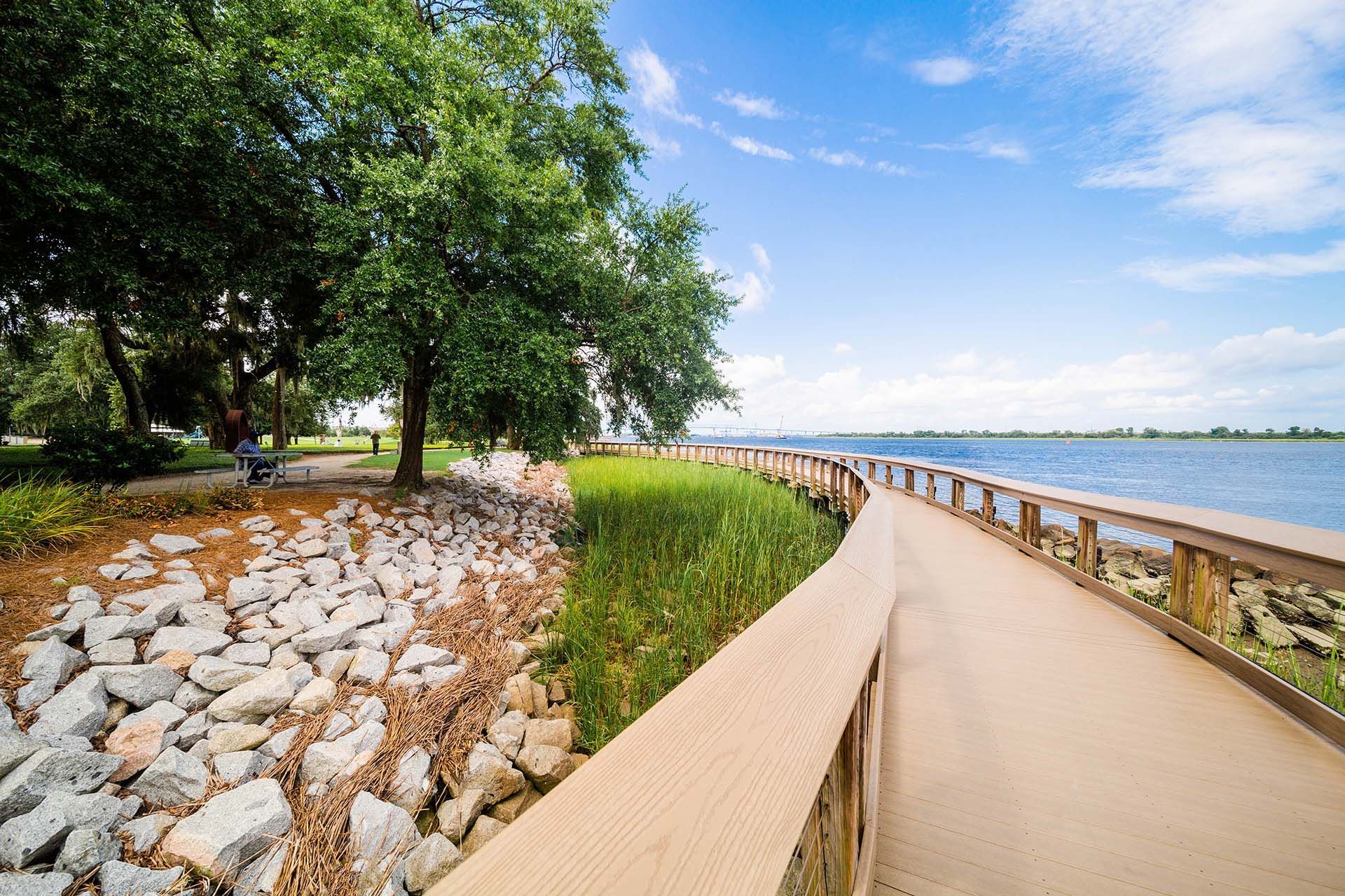 Wooden boardwalk by water, under a tree, with blue sky.