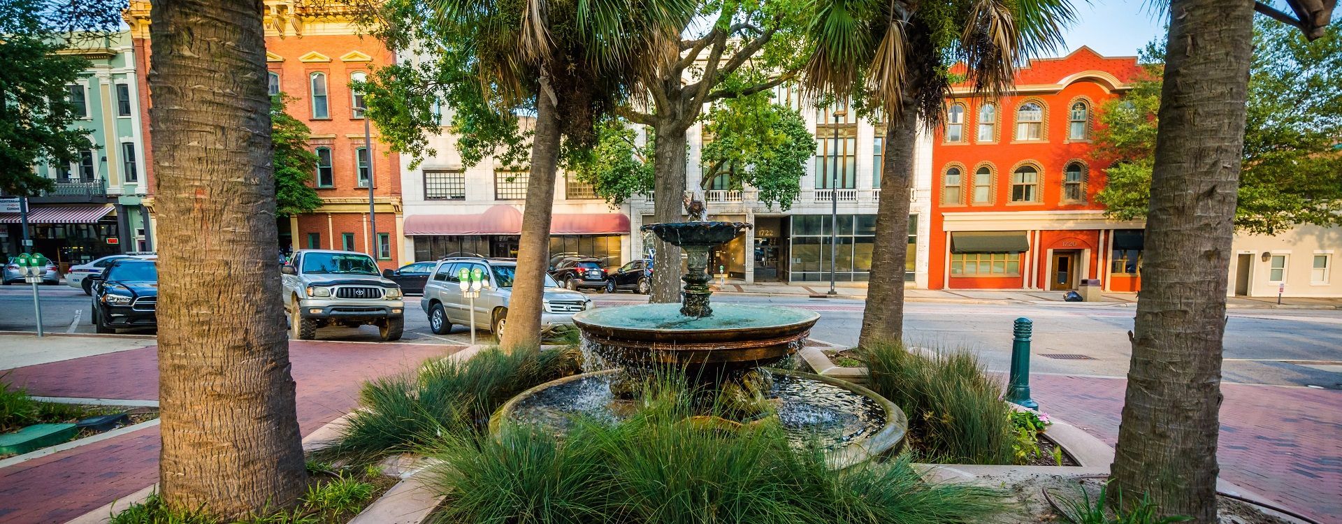A fountain in the middle of a city square surrounded by trees and buildings.