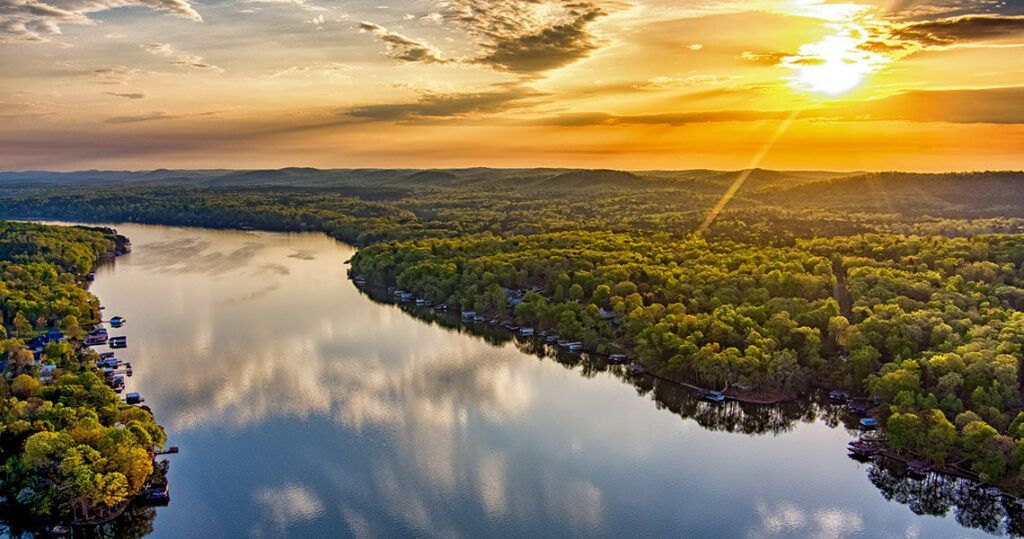 An aerial view of a river surrounded by trees at sunset.