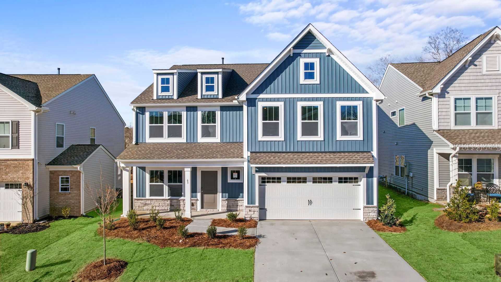 A blue and white house with a large garage is surrounded by other houses.