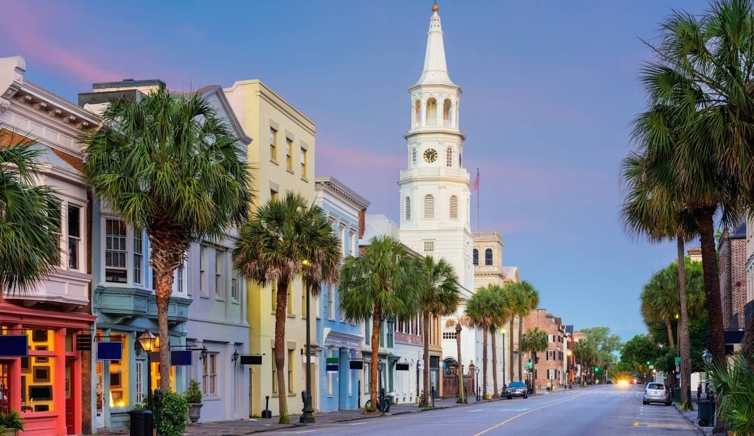 Charleston, South Carolina street with colorful buildings, palm trees, and a church steeple.