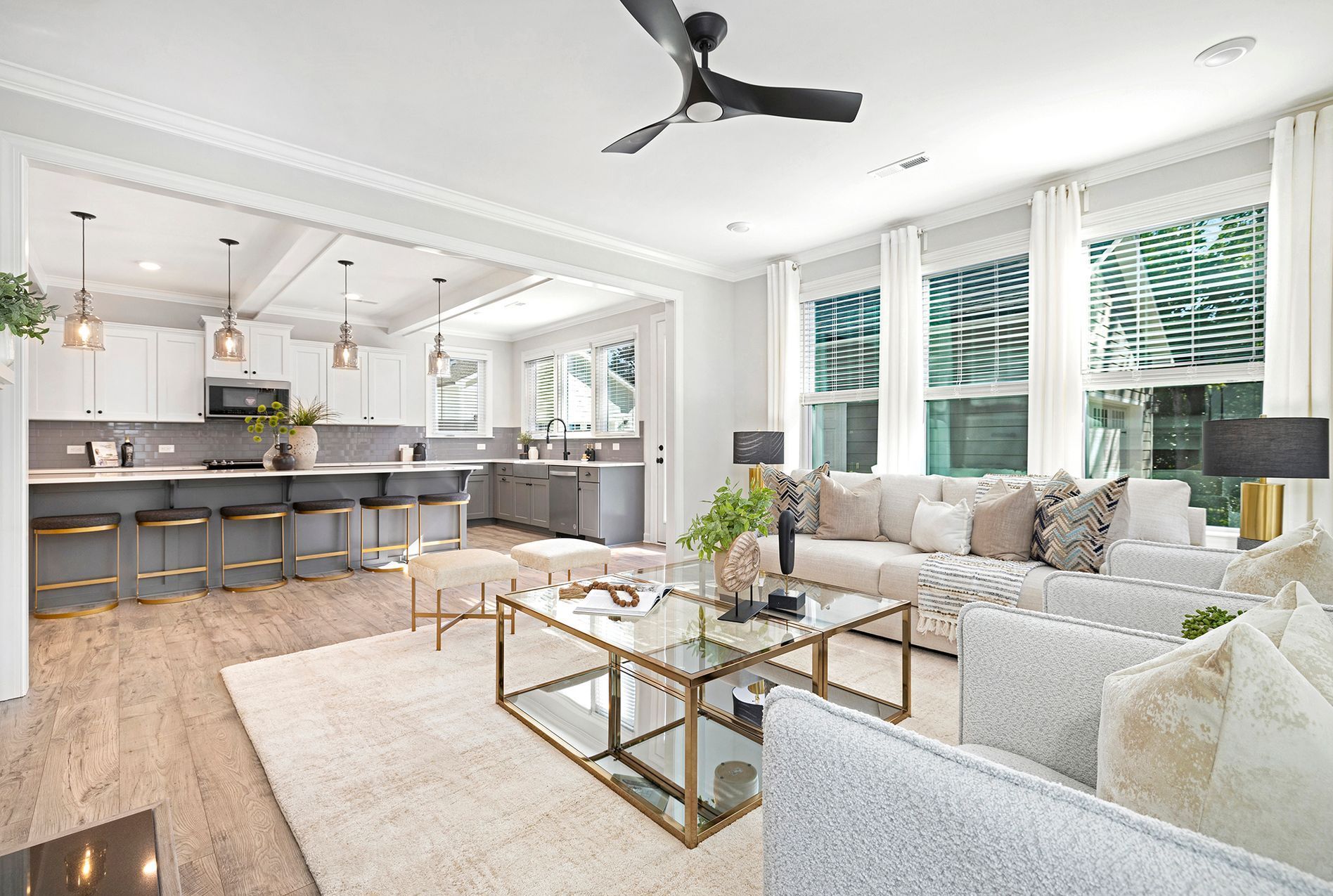 Open-concept living space: kitchen with gray cabinets, living room with white sofa, large windows, and light wood floors.