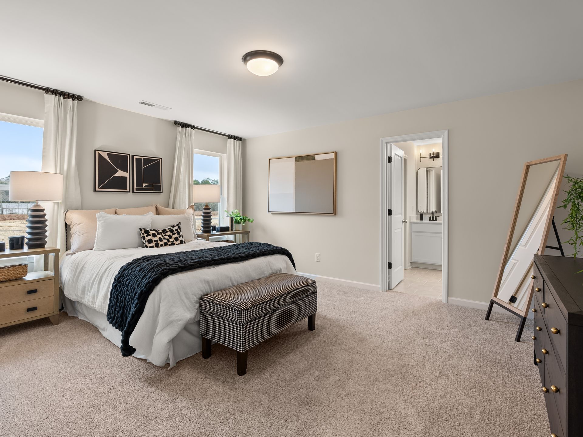A bedroom with a bed , dresser , mirror and ottoman.