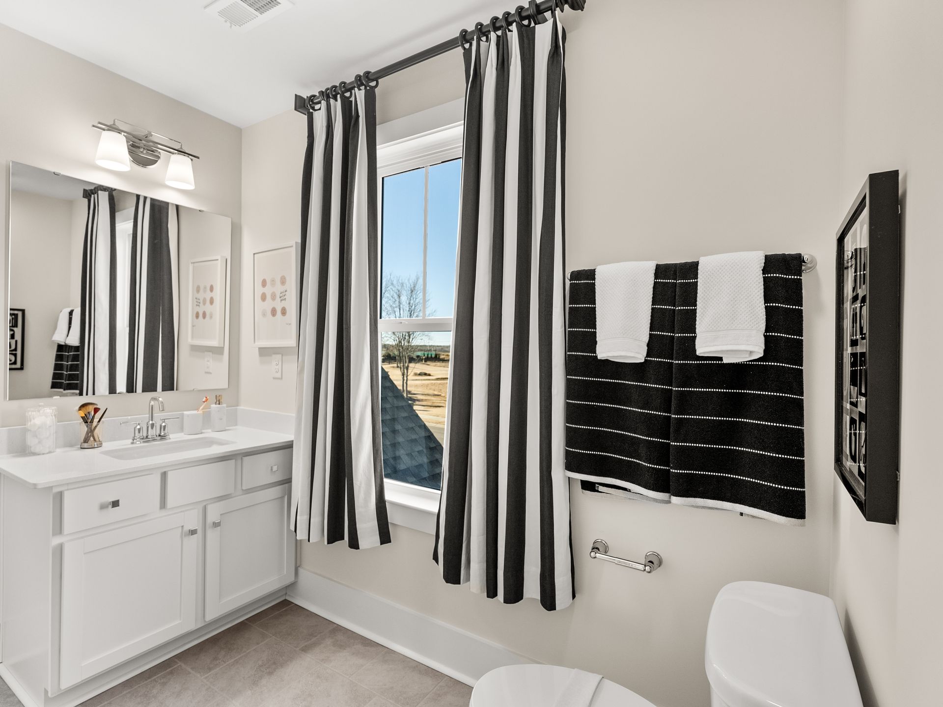 A bathroom with a sink , toilet , mirror and black and white curtains.
