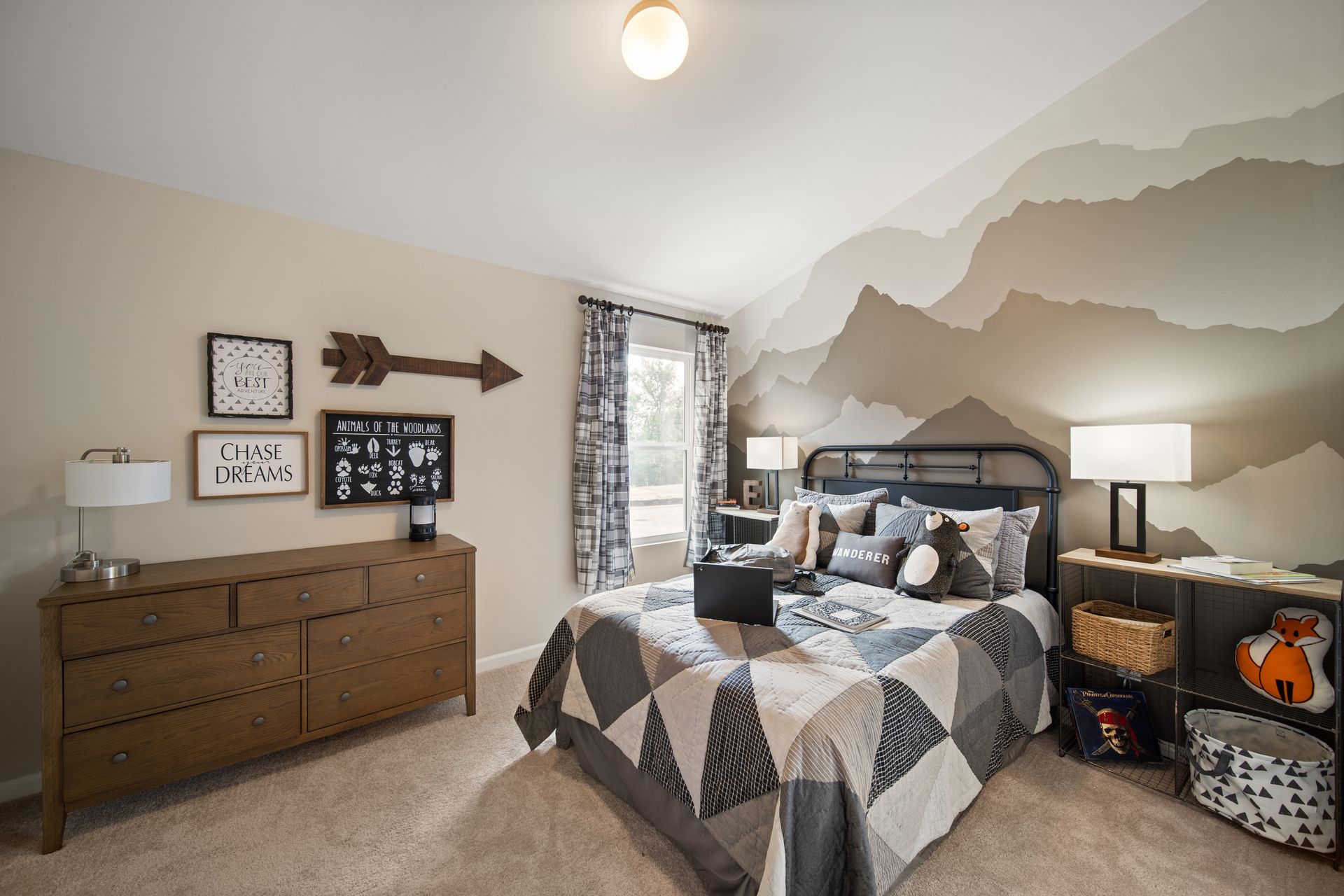 a bedroom with a bed , dresser , lamps and a mountain mural on the wall .