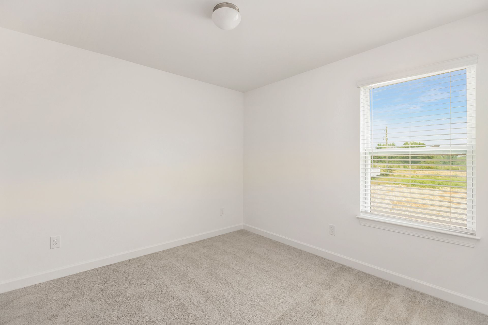 An empty bedroom with a window and blinds.
