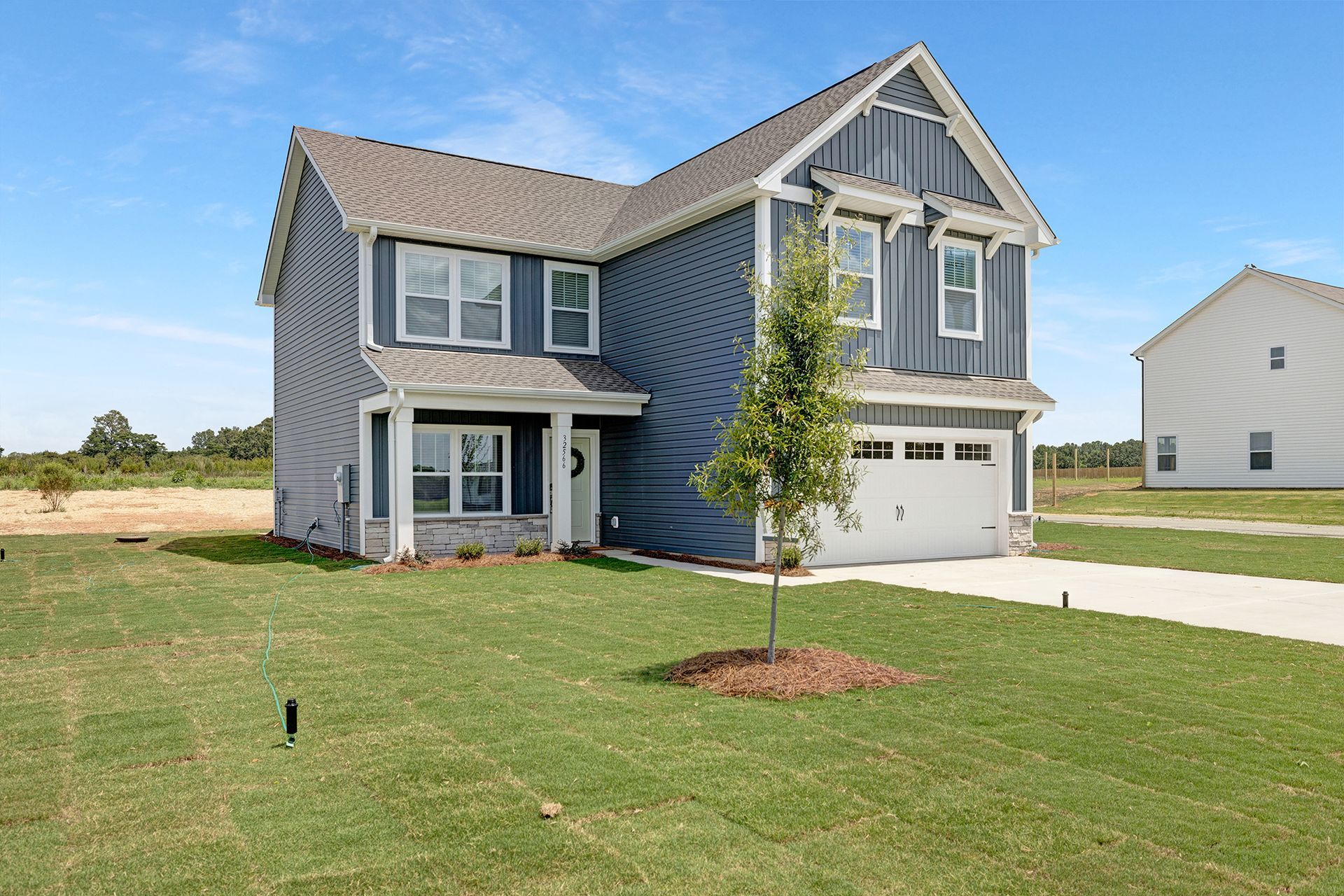 A large blue house with a white garage and a tree in front of it.