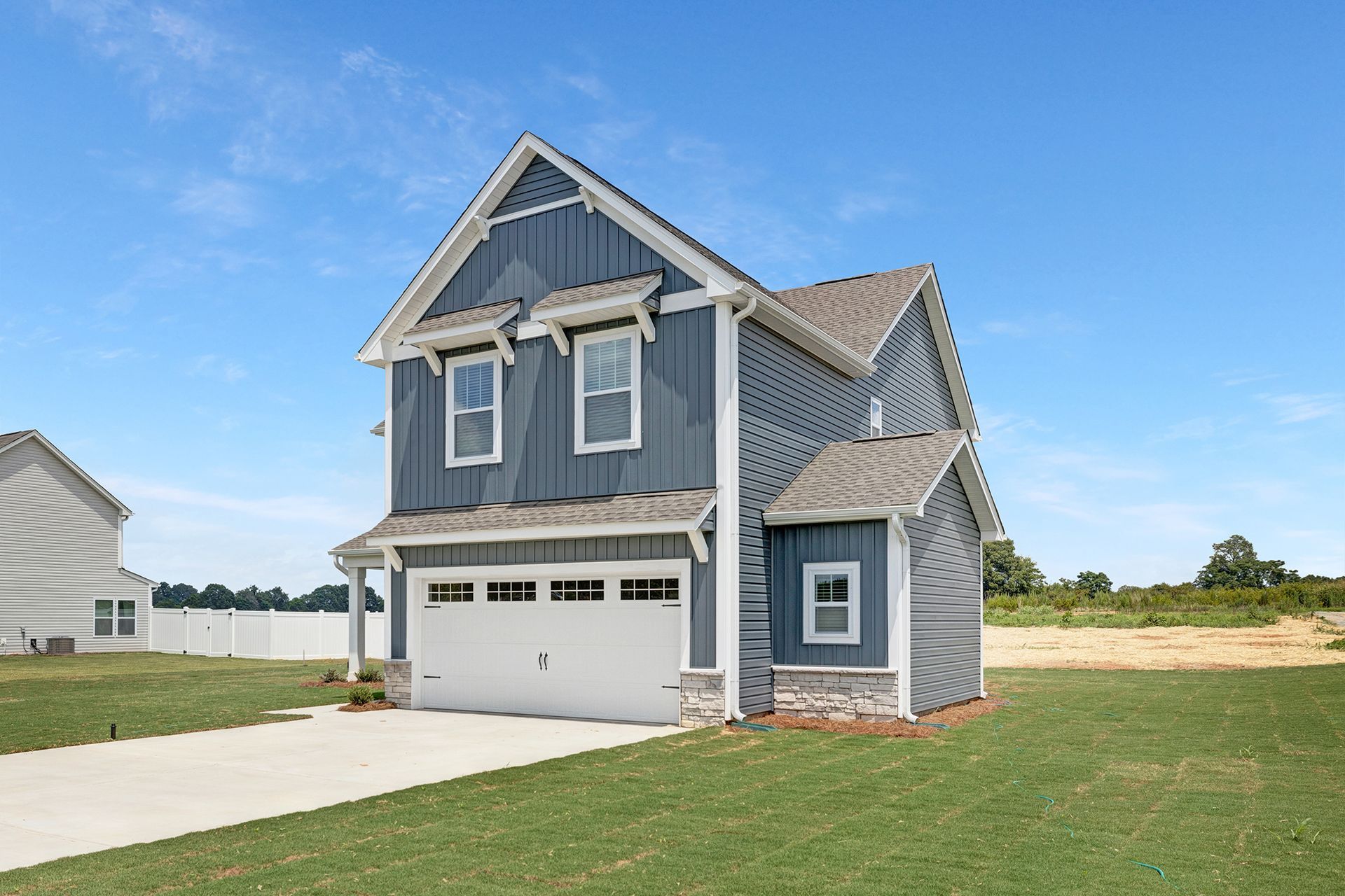 A blue house with a white garage door is sitting on top of a lush green field.