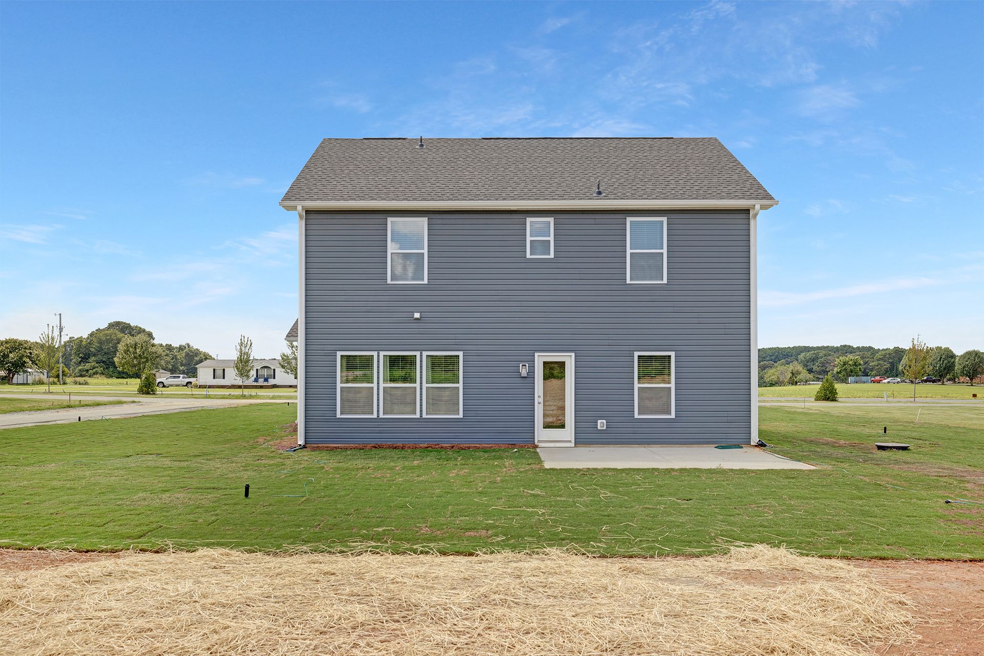 A large gray house is sitting in the middle of a grassy field.