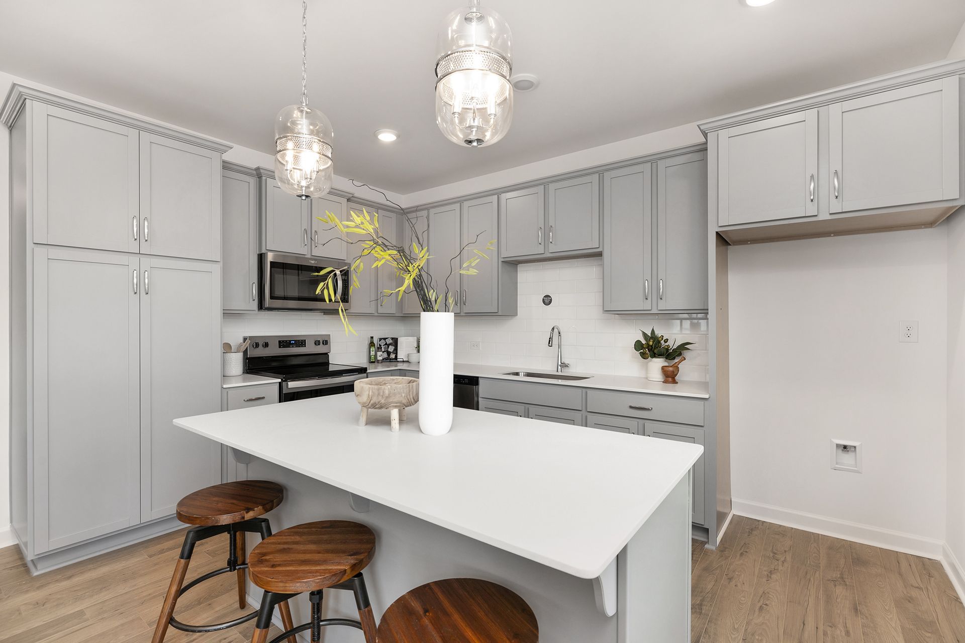 A kitchen with gray cabinets , white counter tops , stools and a large island.
