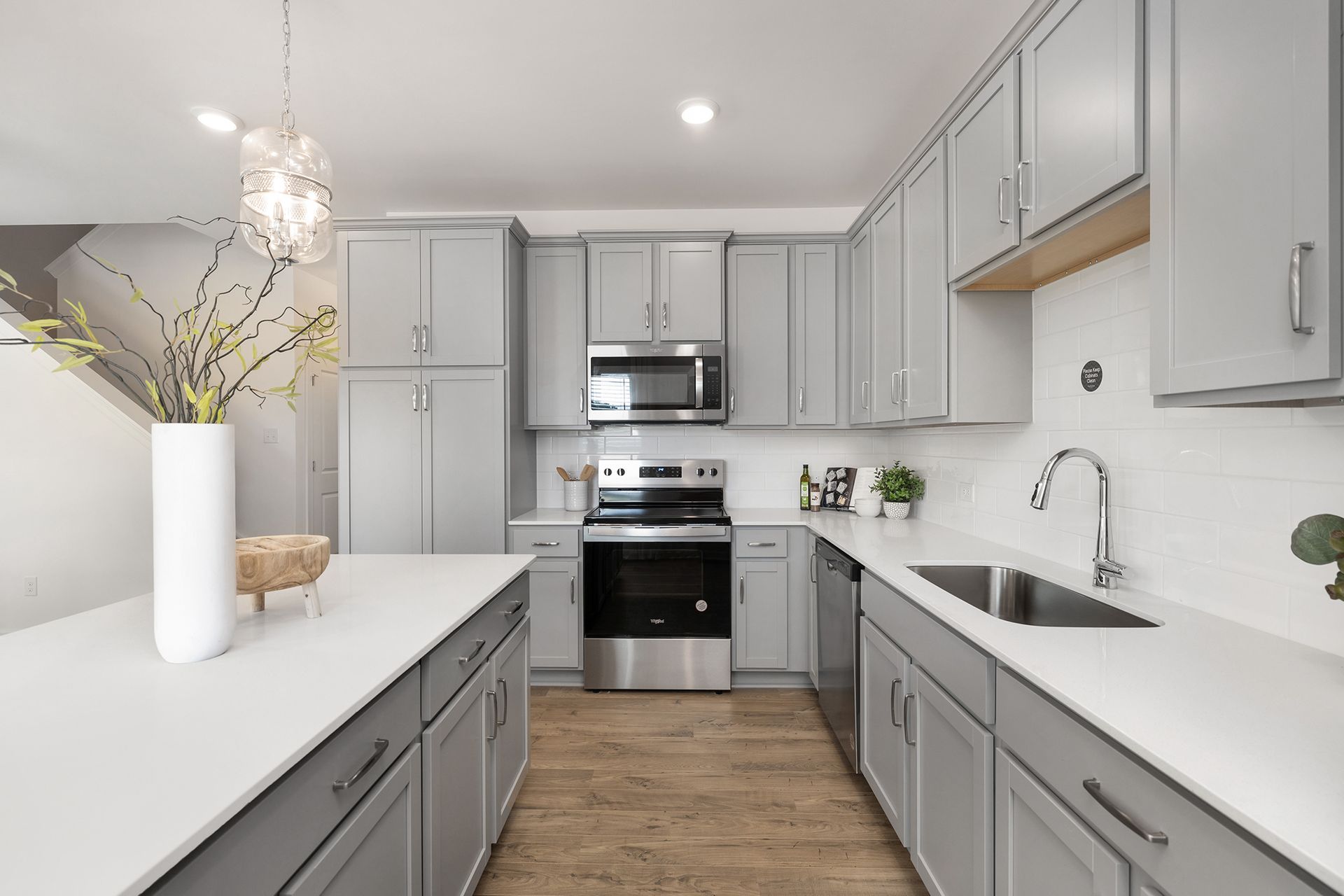 A kitchen with gray cabinets , white counter tops , stainless steel appliances and a sink.