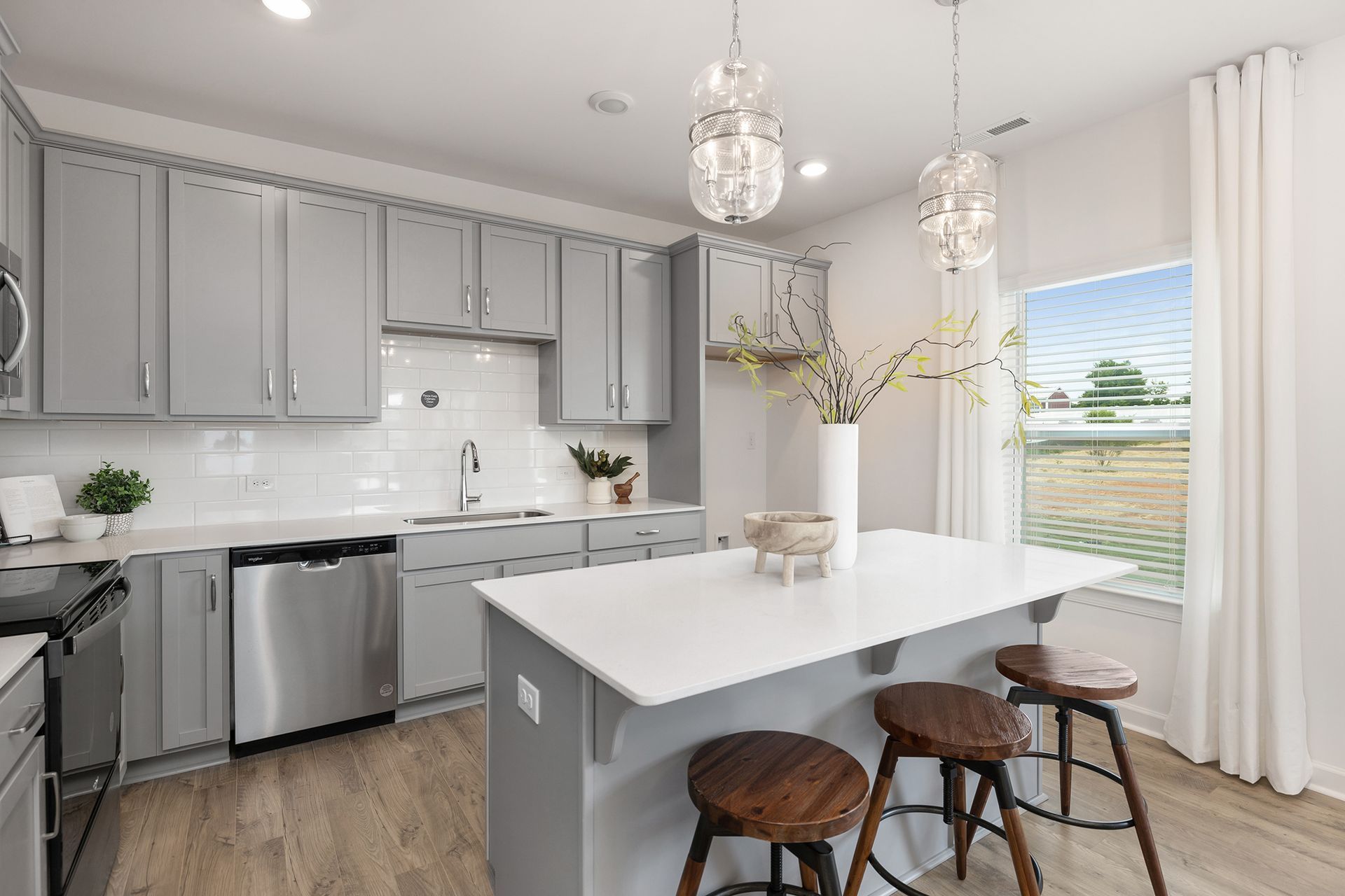 A kitchen with gray cabinets , stainless steel appliances , and a large island.