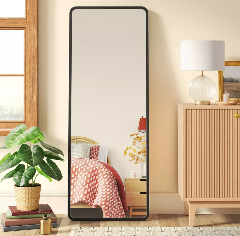 A full length mirror is hanging on a wall in a bedroom.