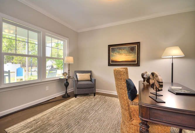 A home office with a desk , chair , lamp and two windows.