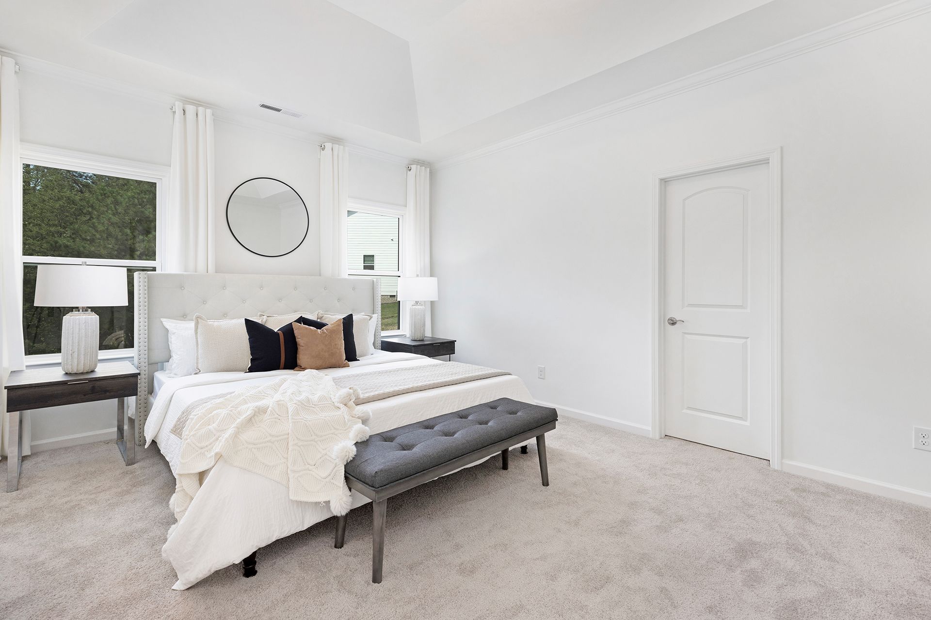 A bedroom with a bed , bench , lamps , and a window.