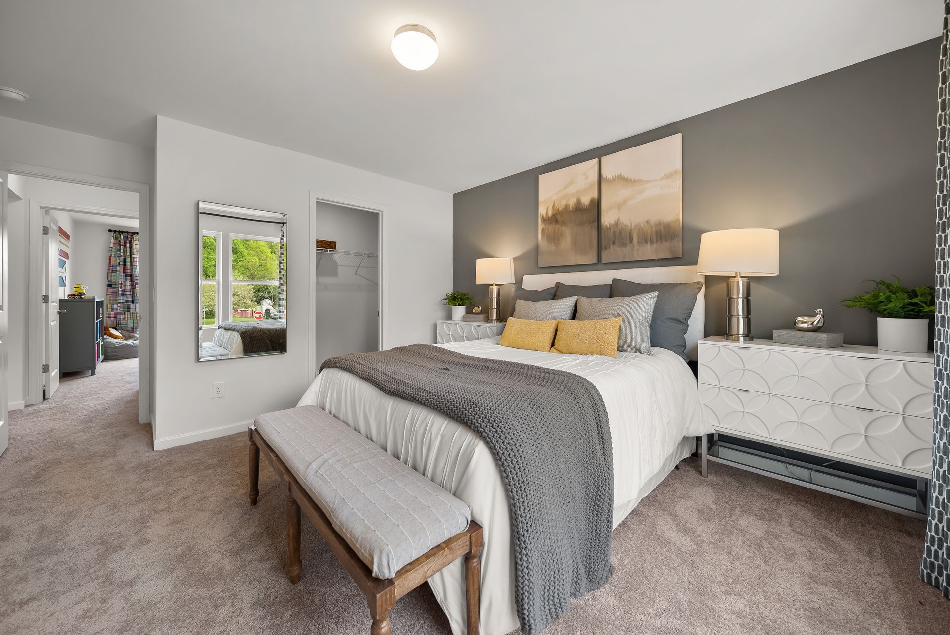 A bedroom with a large bed , dresser , bench and mirror.