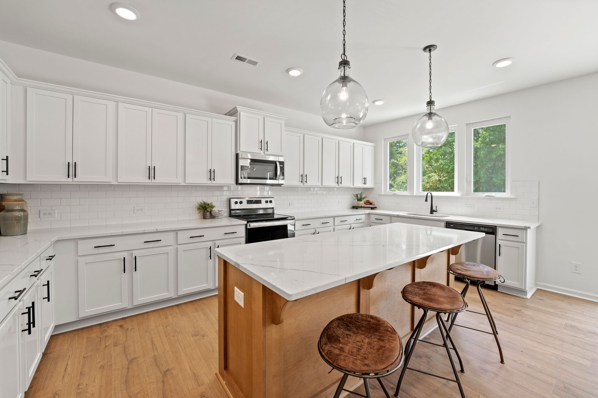 A kitchen with white cabinets , a large island , stools and a stove.