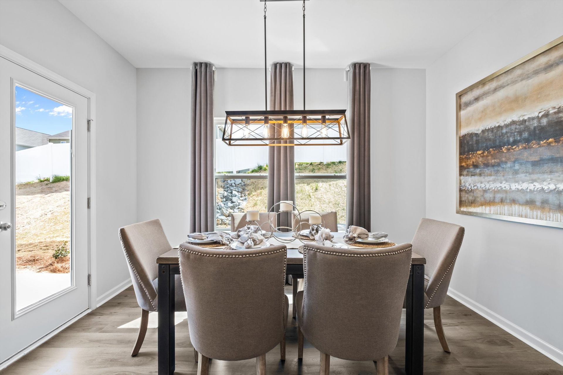 A dining room with a table and chairs and a painting on the wall.