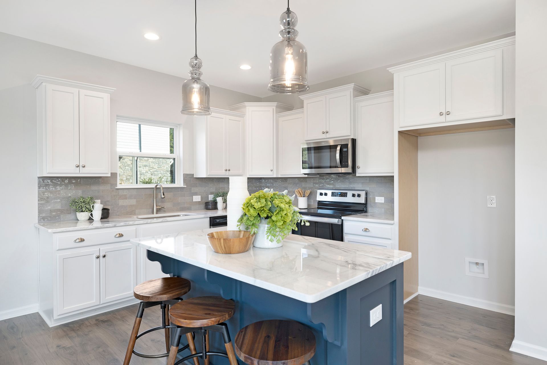 A kitchen with white cabinets , a blue island , and stools.