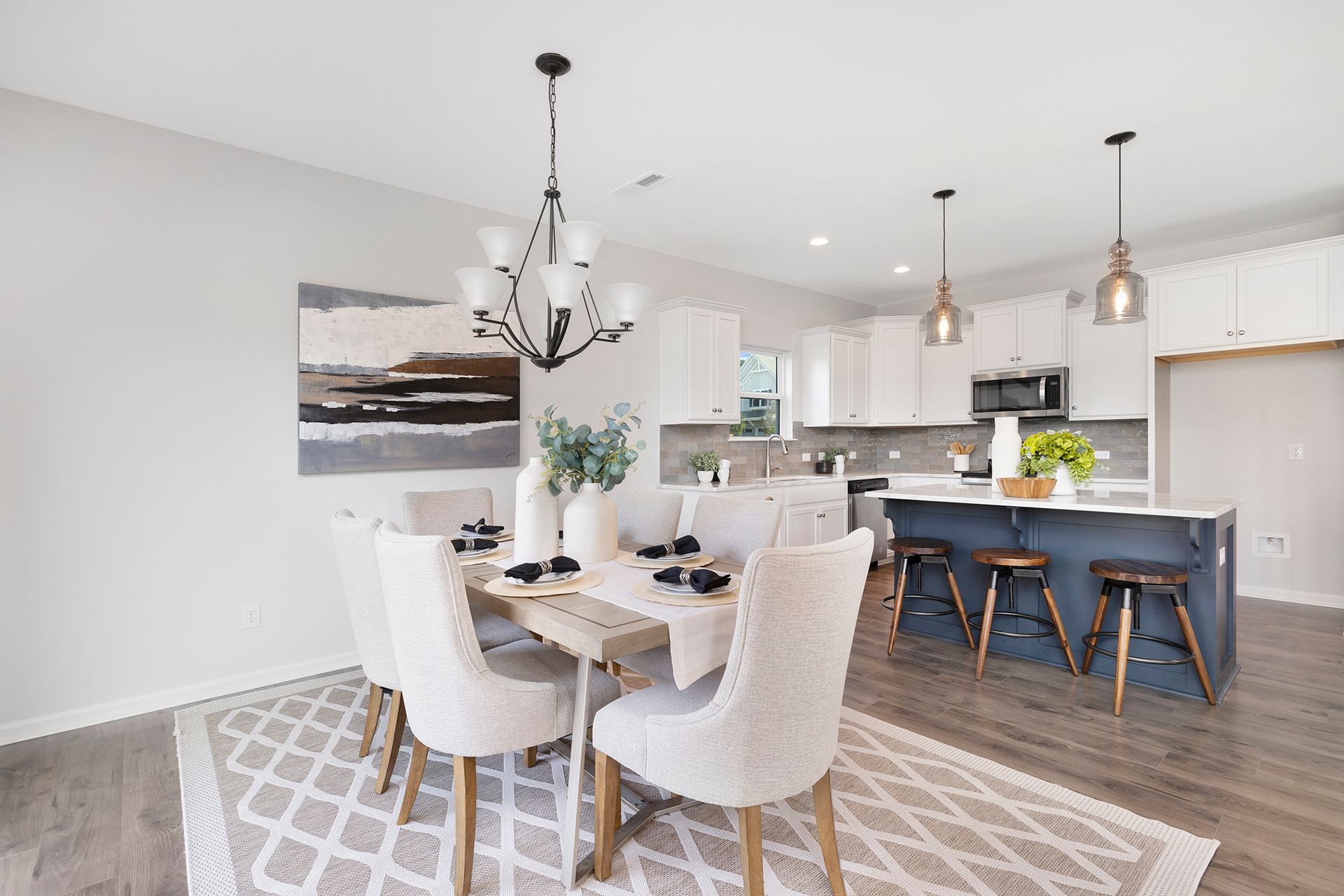 A dining room with a table and chairs and a kitchen in the background.