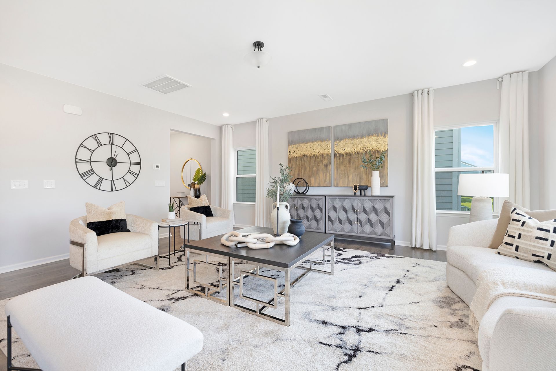 A living room with white furniture and a large clock on the wall.