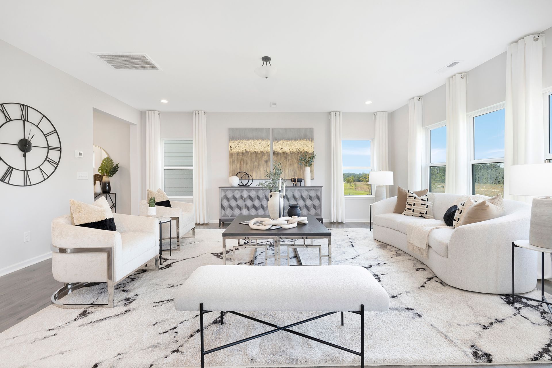 A living room with white furniture and a large clock on the wall.