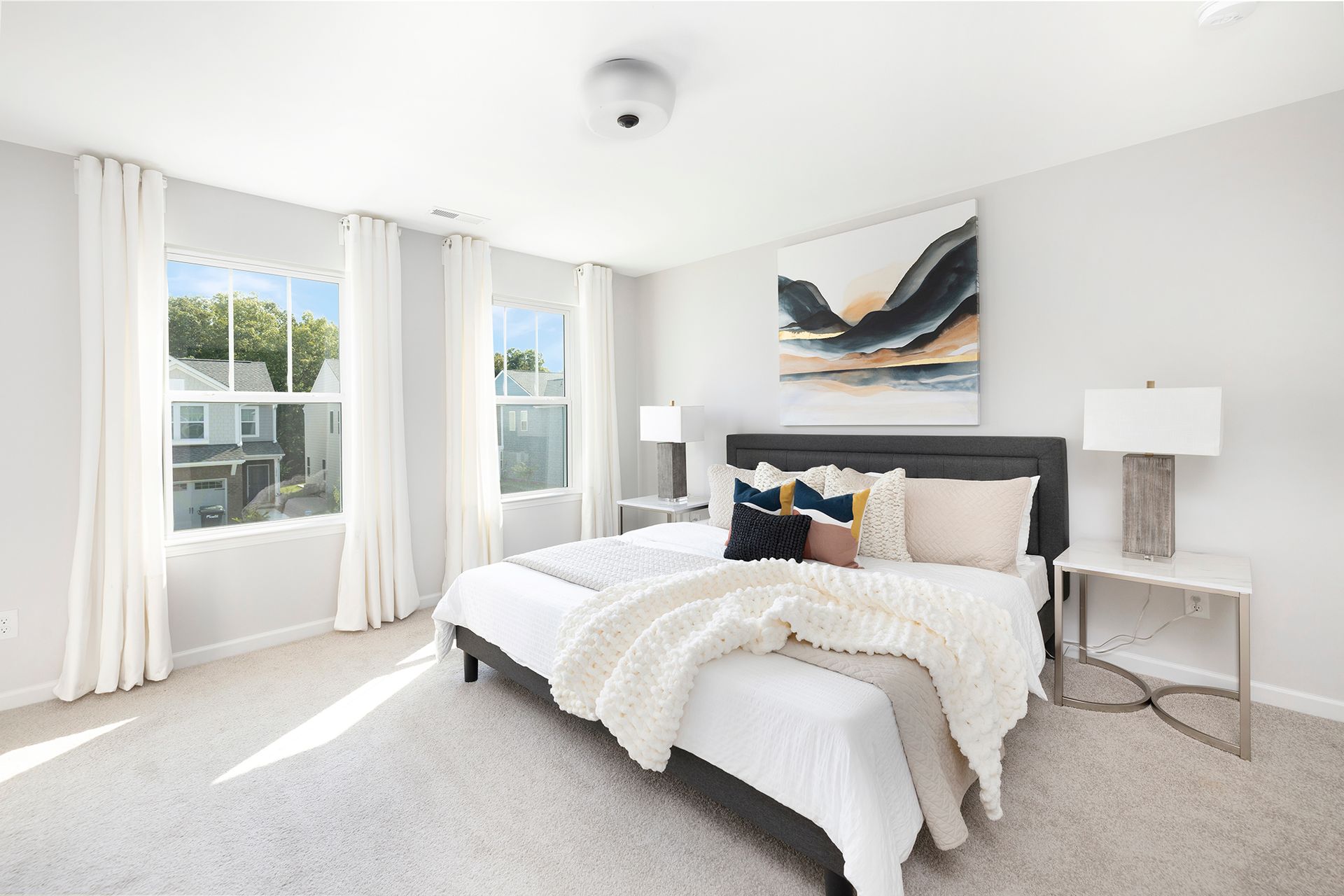 A bedroom with a large bed , two windows and a painting on the wall.