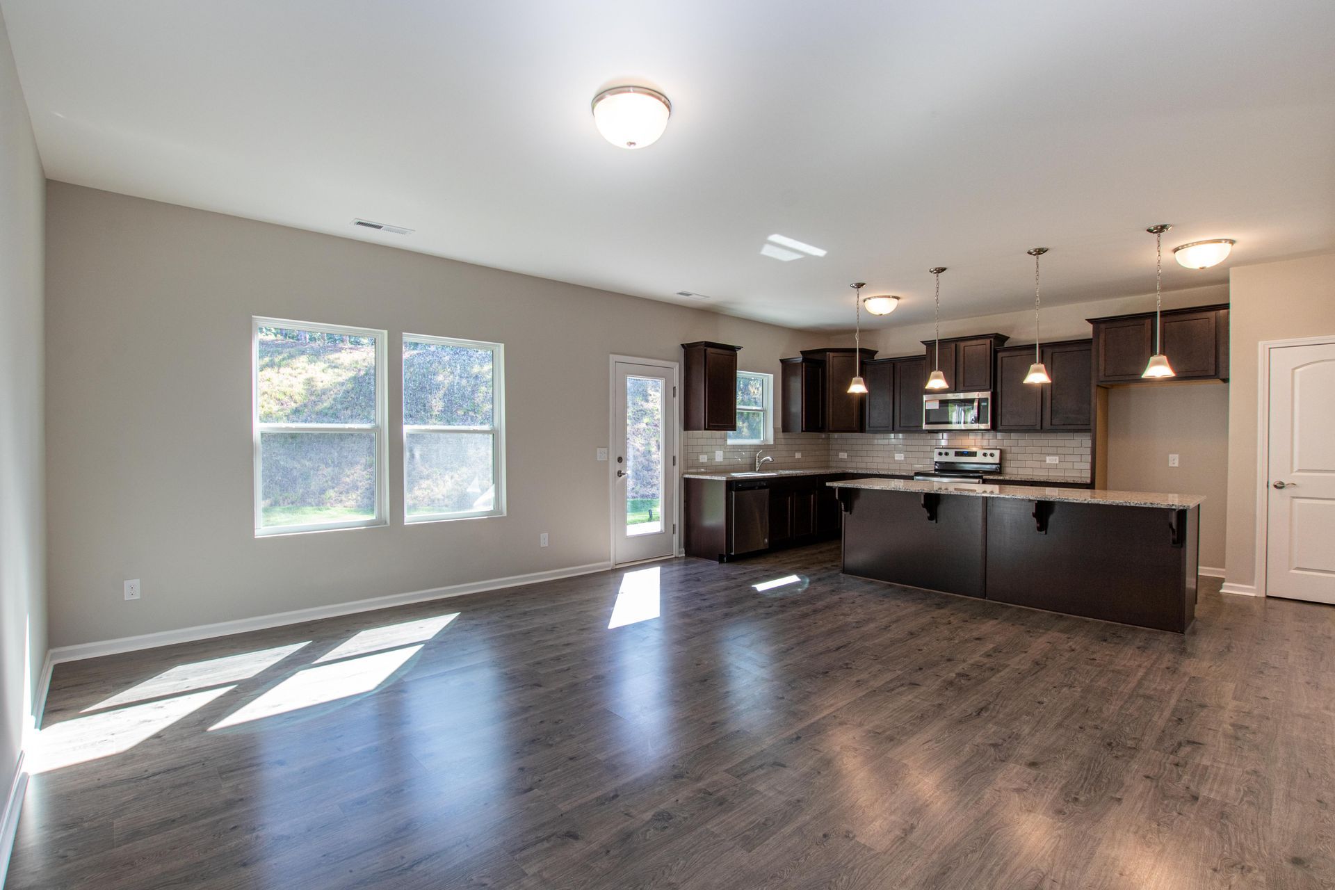 An empty living room with hardwood floors and a kitchen in a new home.
