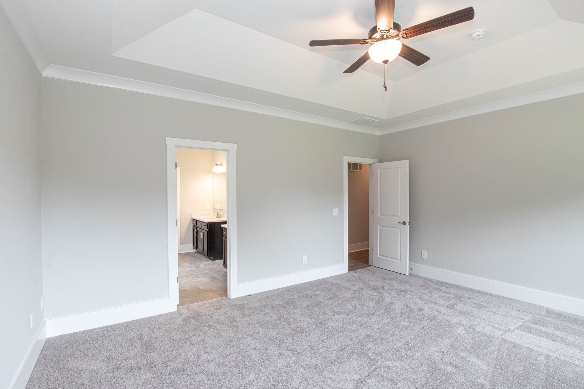 An empty bedroom with a ceiling fan and gray carpet.