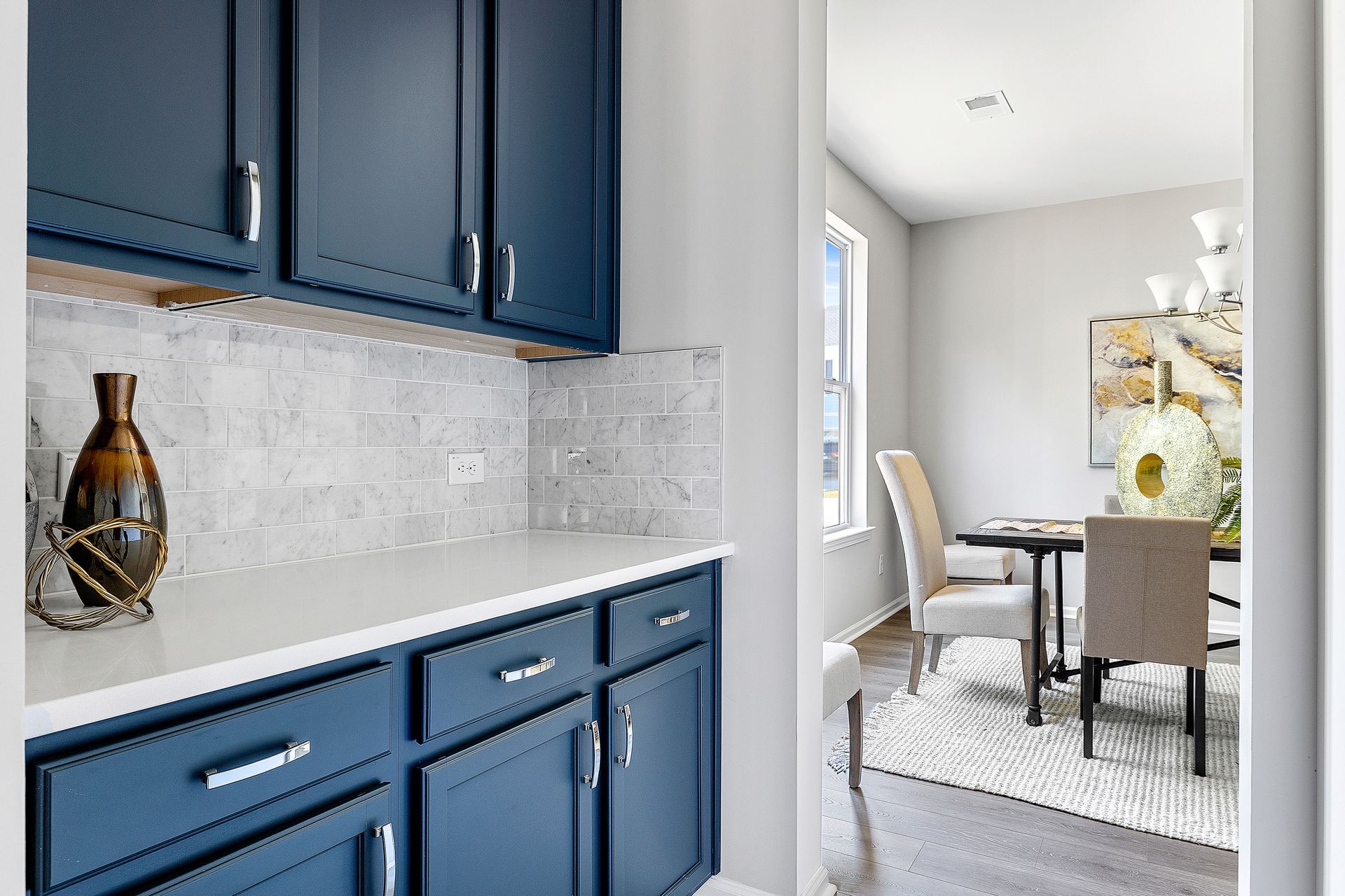 A kitchen with blue cabinets and white counter tops and a dining room with a table and chairs.