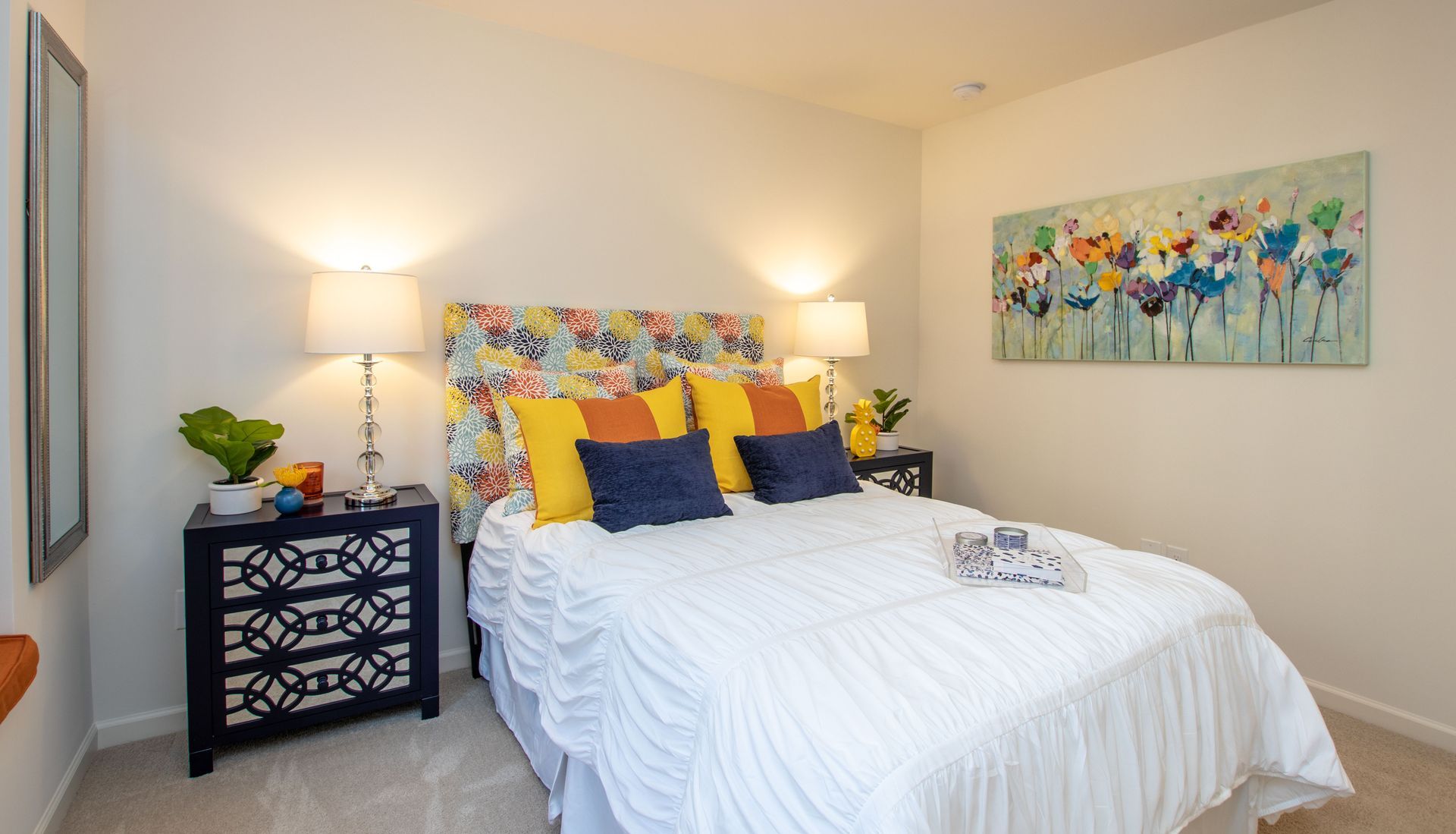 A bedroom with a bed , nightstand , lamps and a painting on the wall.