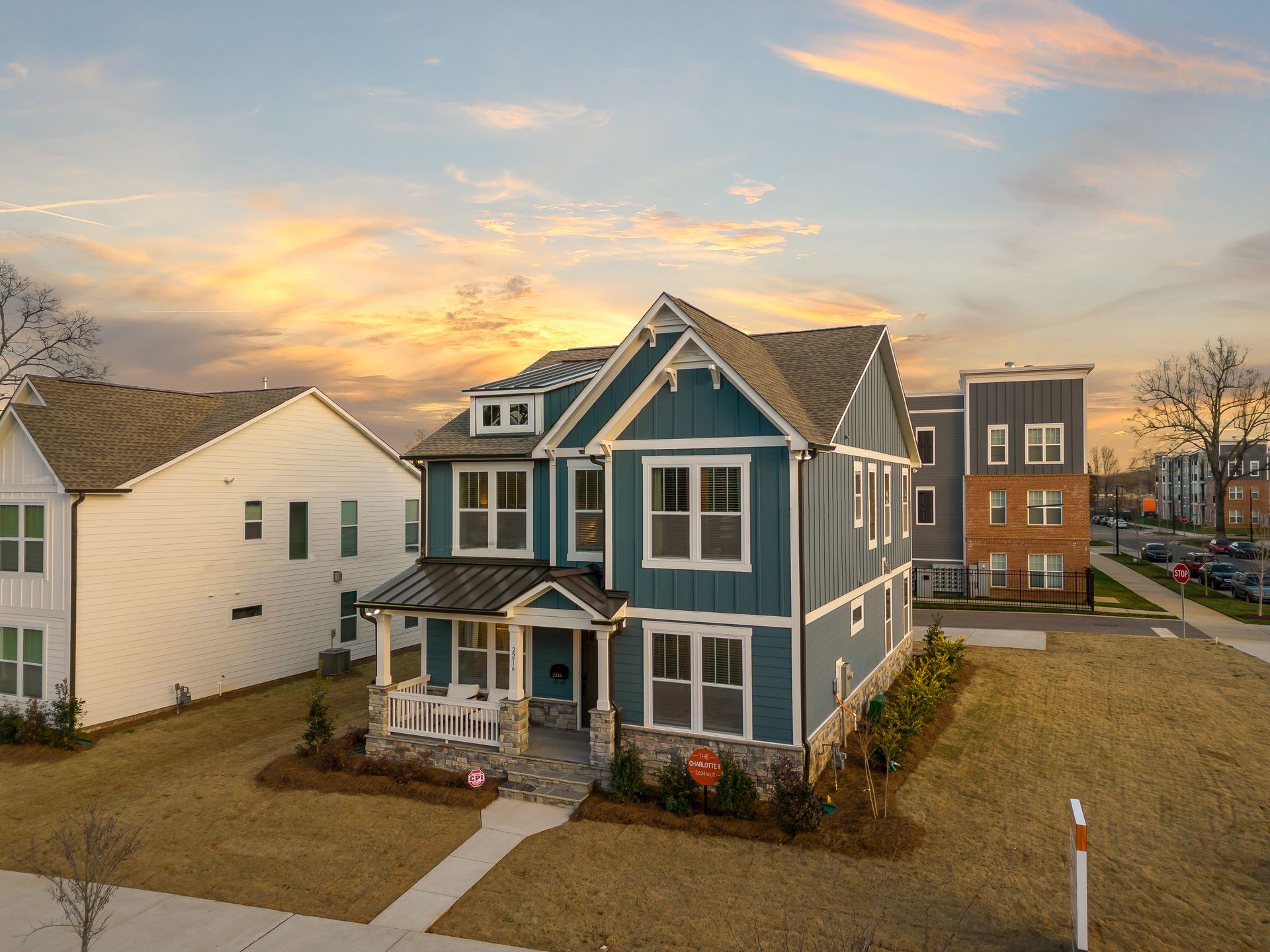 An aerial view of a blue and white house in a residential neighborhood at sunset.