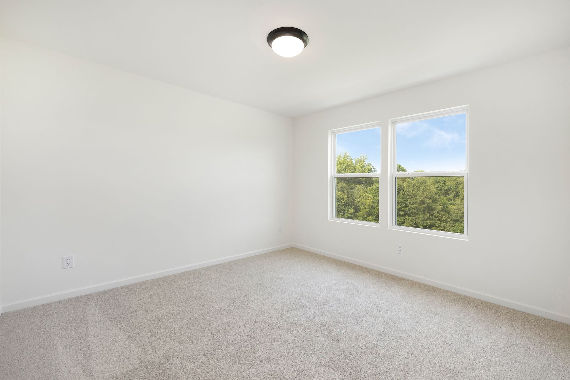 An empty bedroom with two windows and a ceiling light.