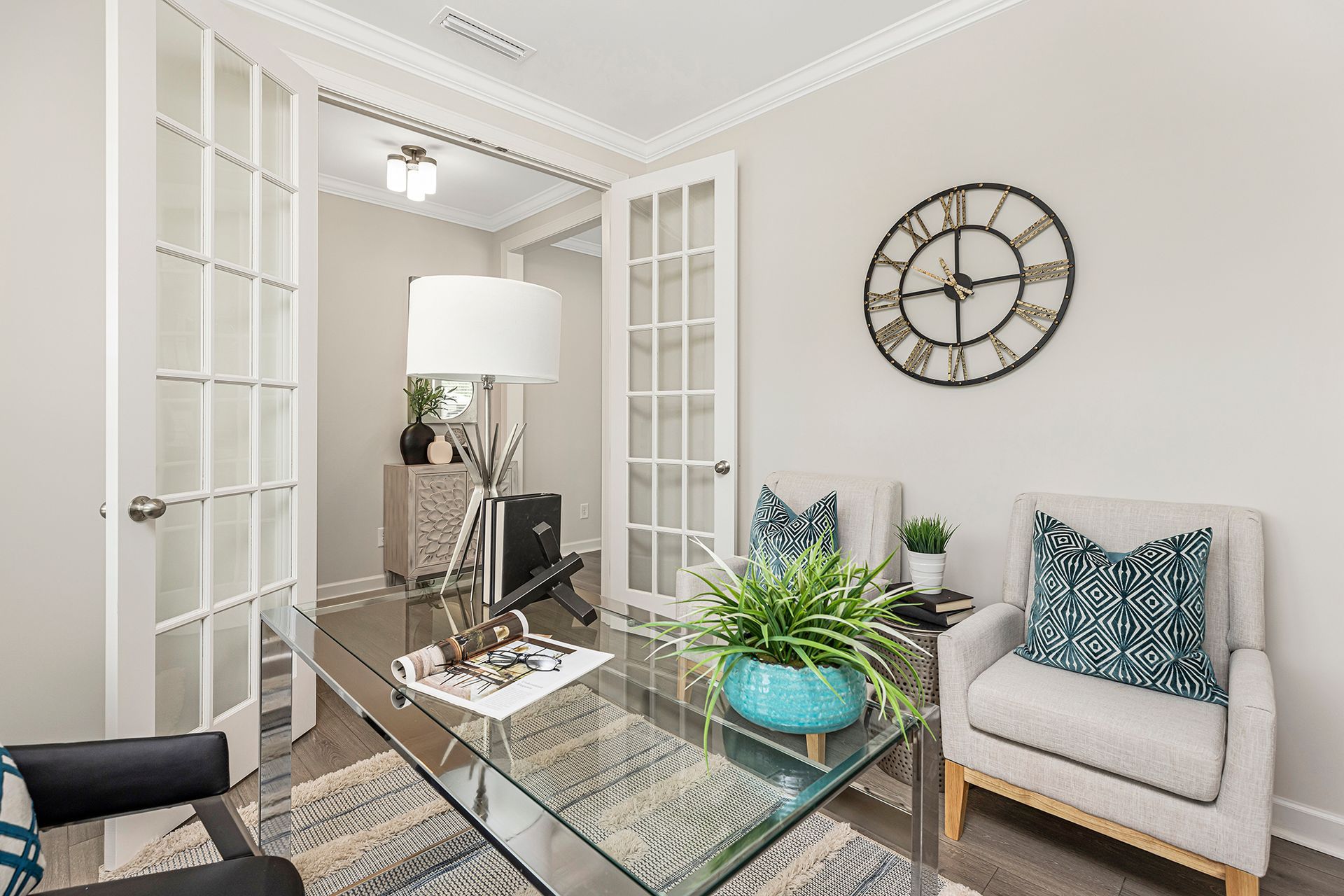 A home office with a glass desk , chair and clock on the wall.