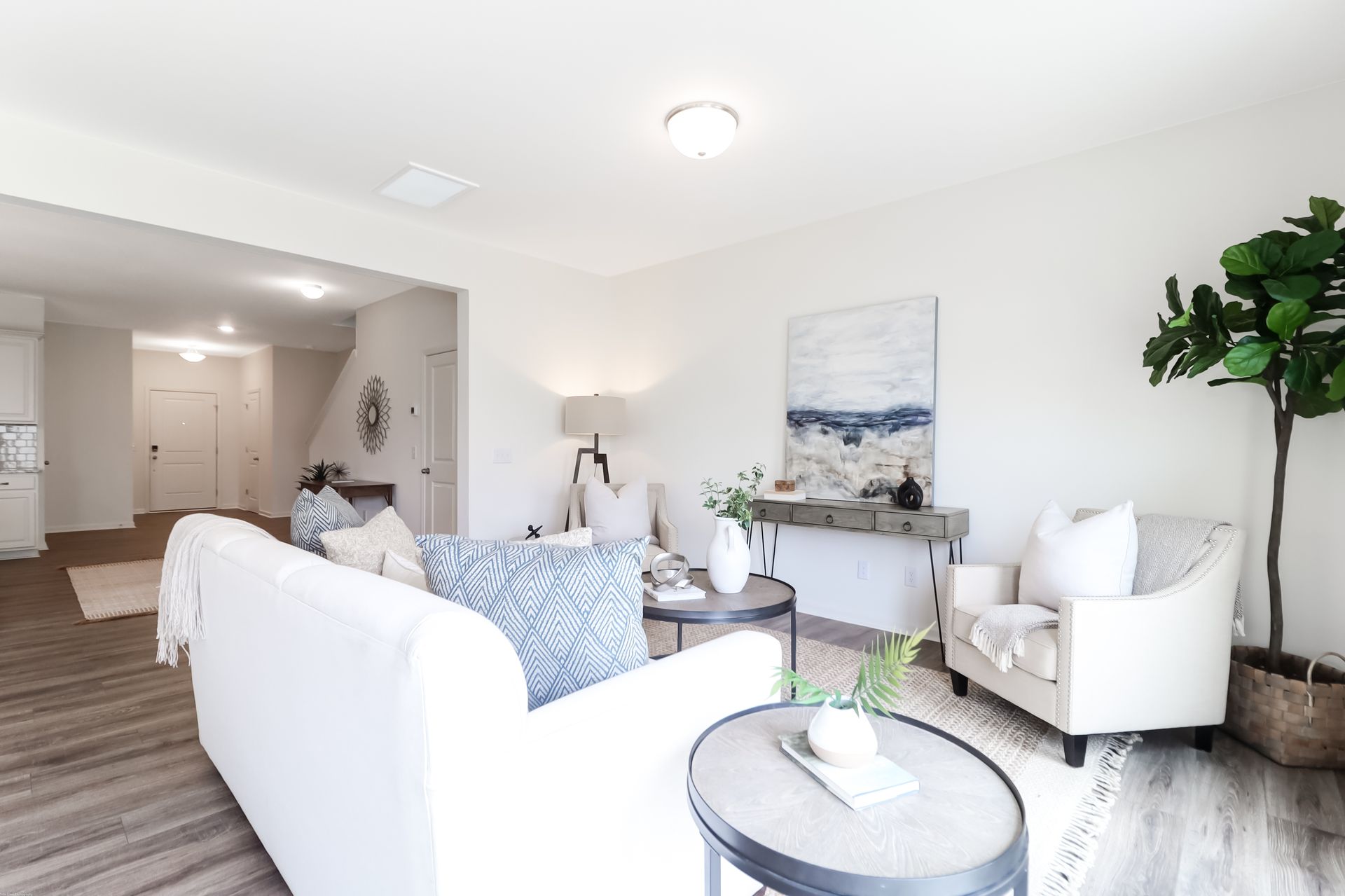 A living room with a white couch , two chairs , a table and a plant.