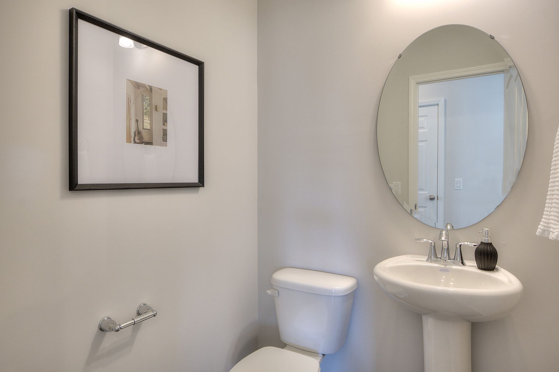 A bathroom with a toilet , sink , mirror and picture on the wall.