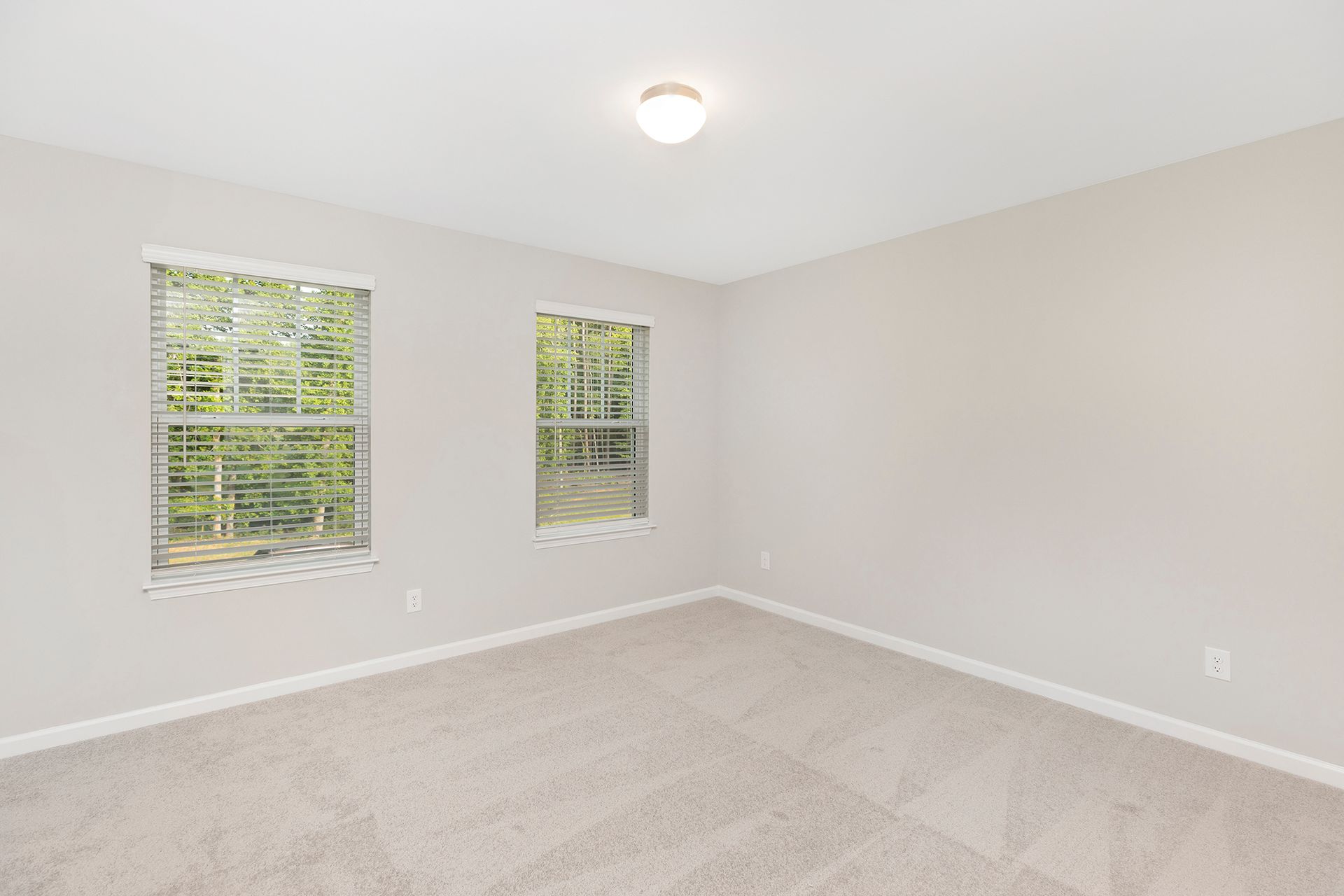 An empty bedroom with two windows and a ceiling light.