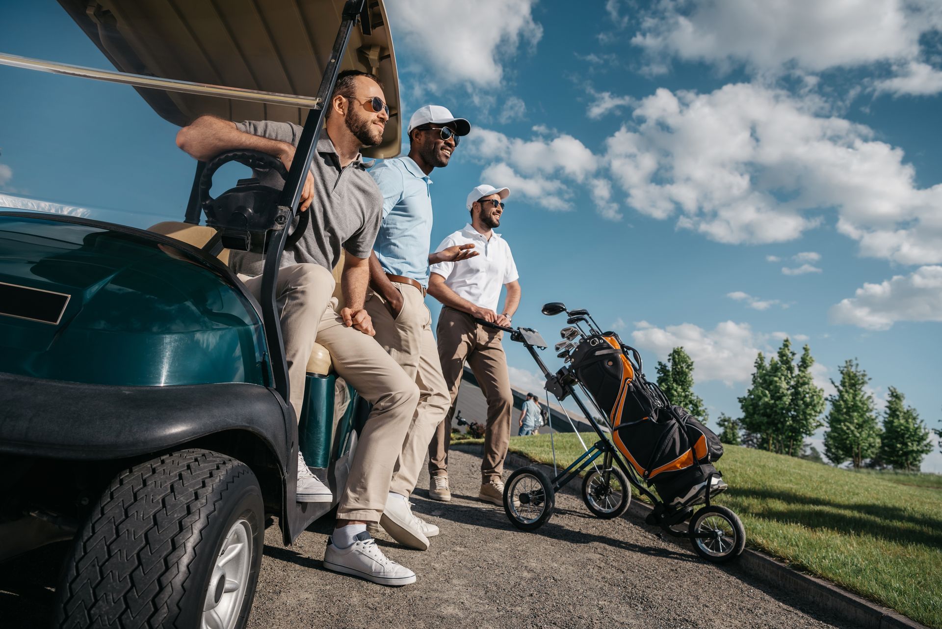 Three men are standing next to a golf cart on a golf course.