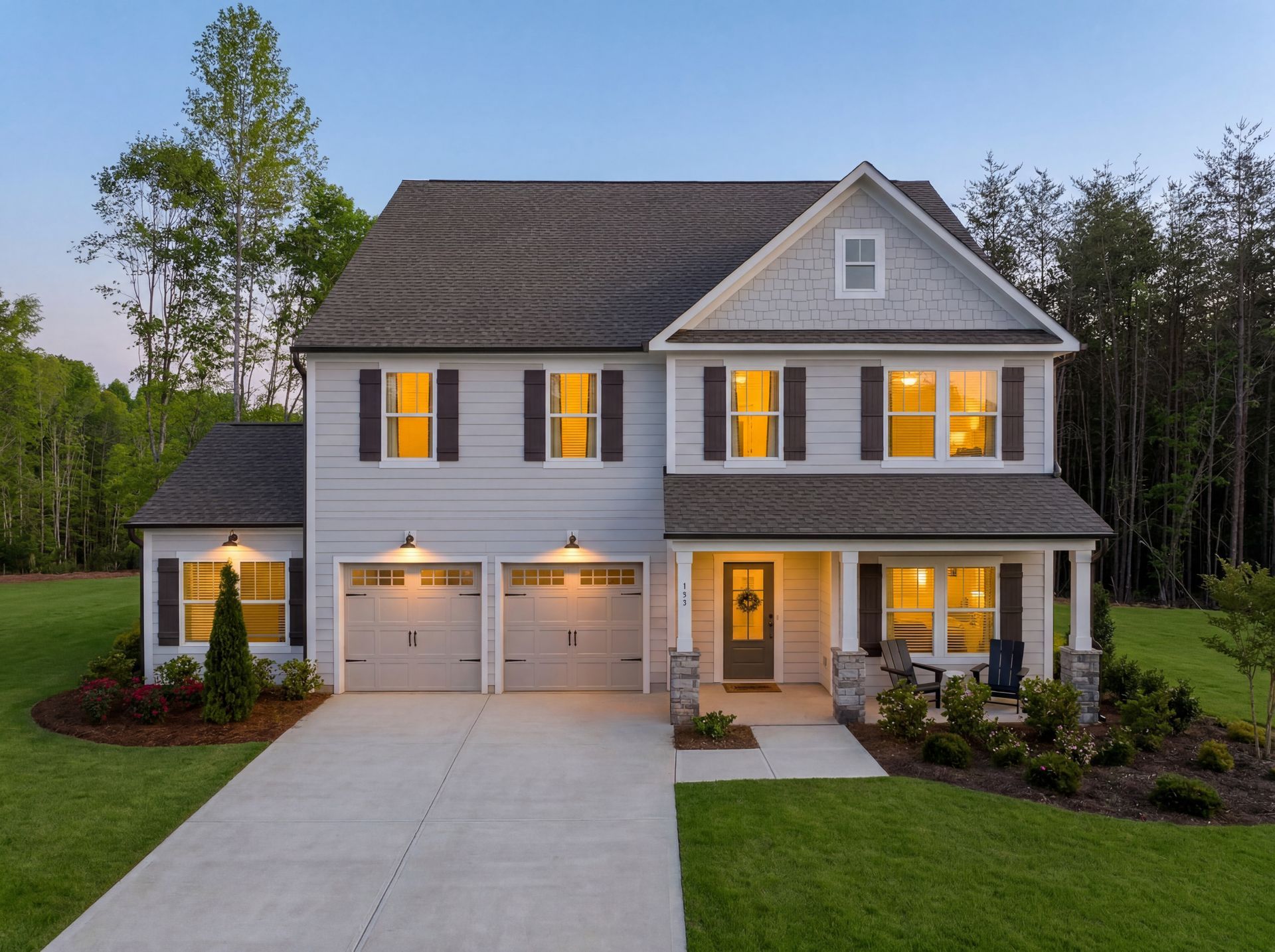 Two-story house with gray siding, white trim, and two-car garage, set on a grassy lot with driveway.