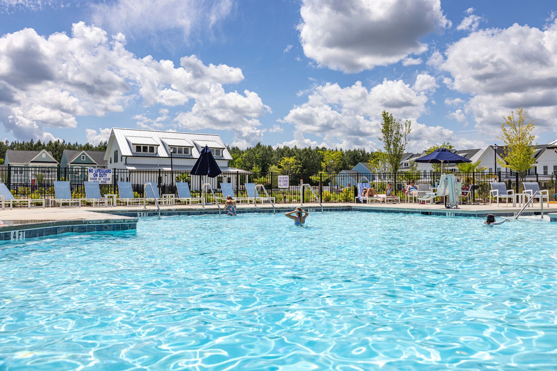 A large swimming pool surrounded by chairs and umbrellas on a sunny day.