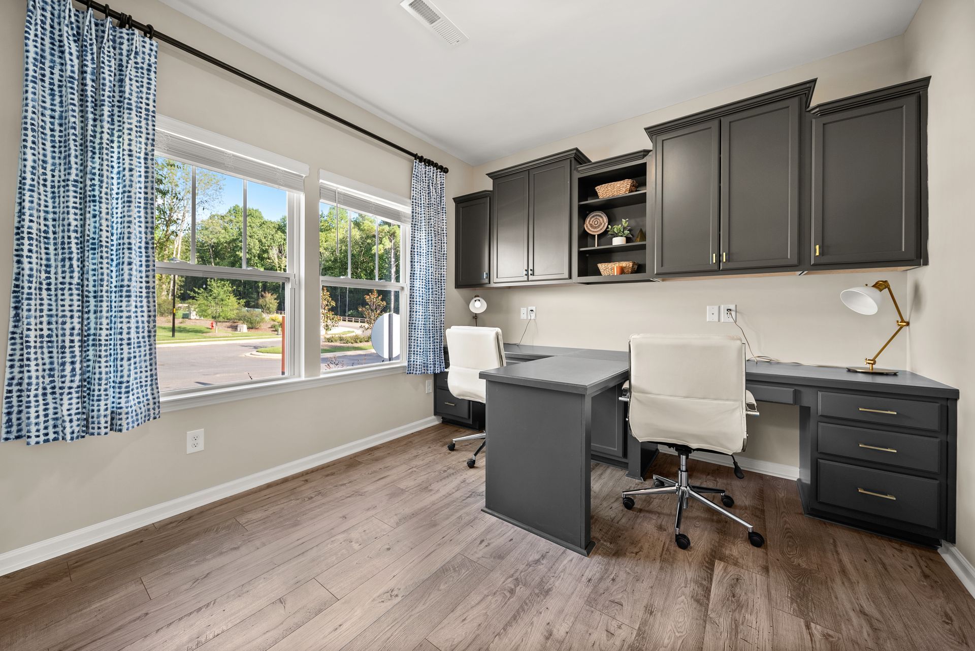 A home office with a desk , chairs , cabinets and a window.