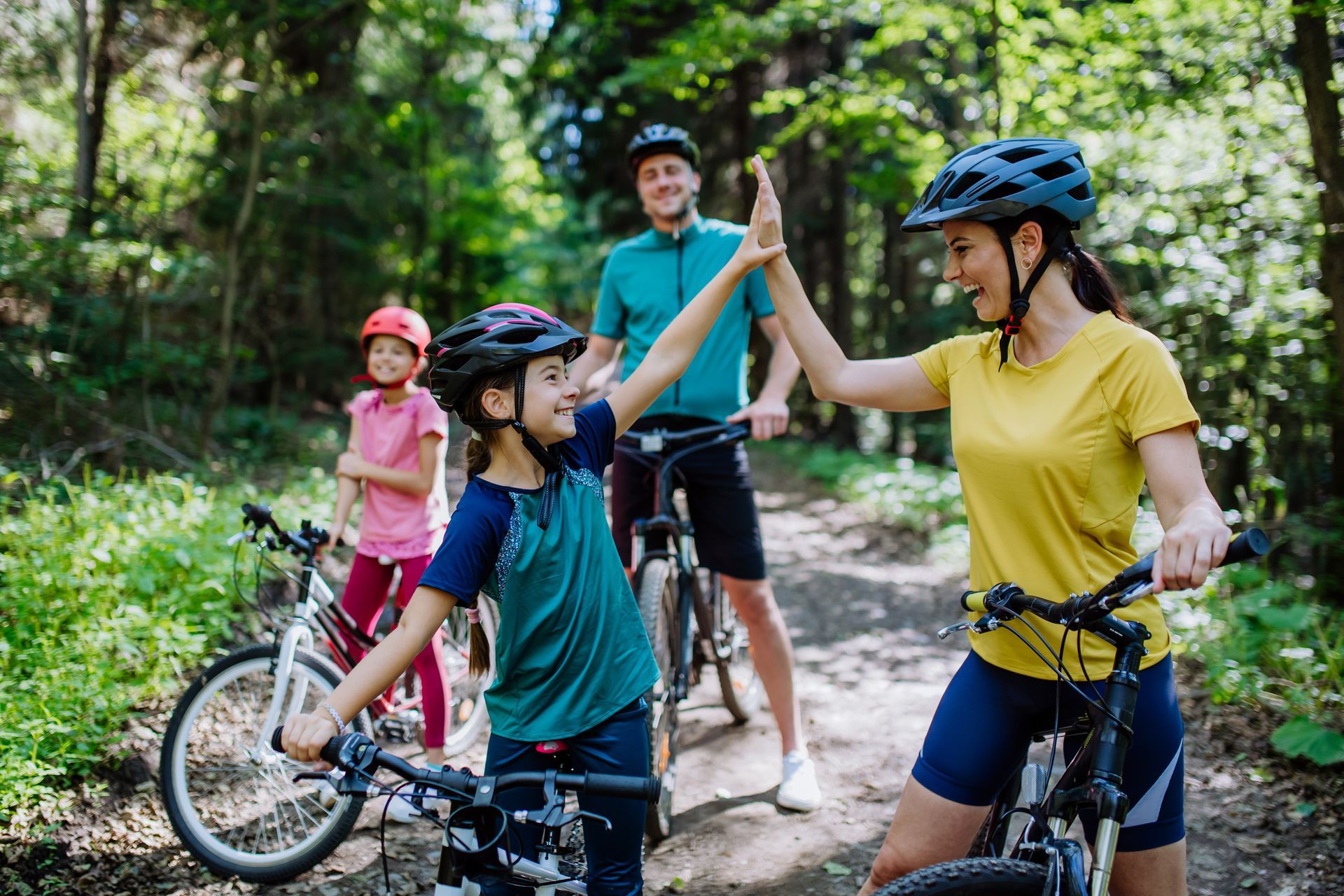 A family is riding bikes in the woods and giving each other a high five.